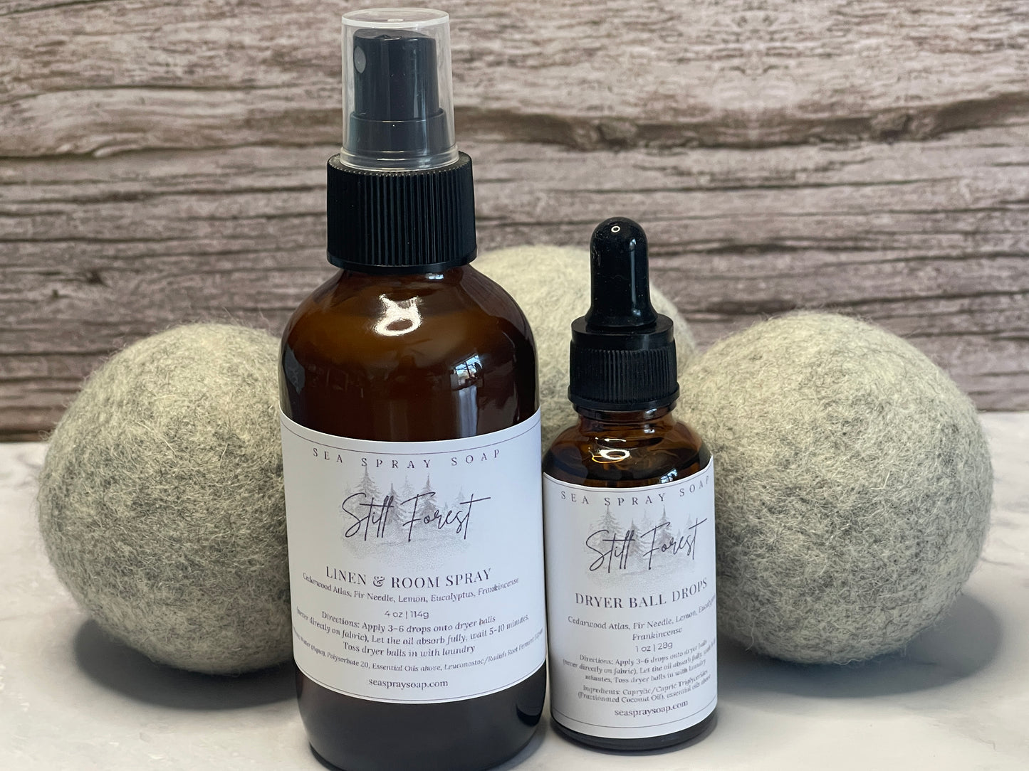 Two bottles of 'Still Forest' products on a wooden surface with dryer balls.