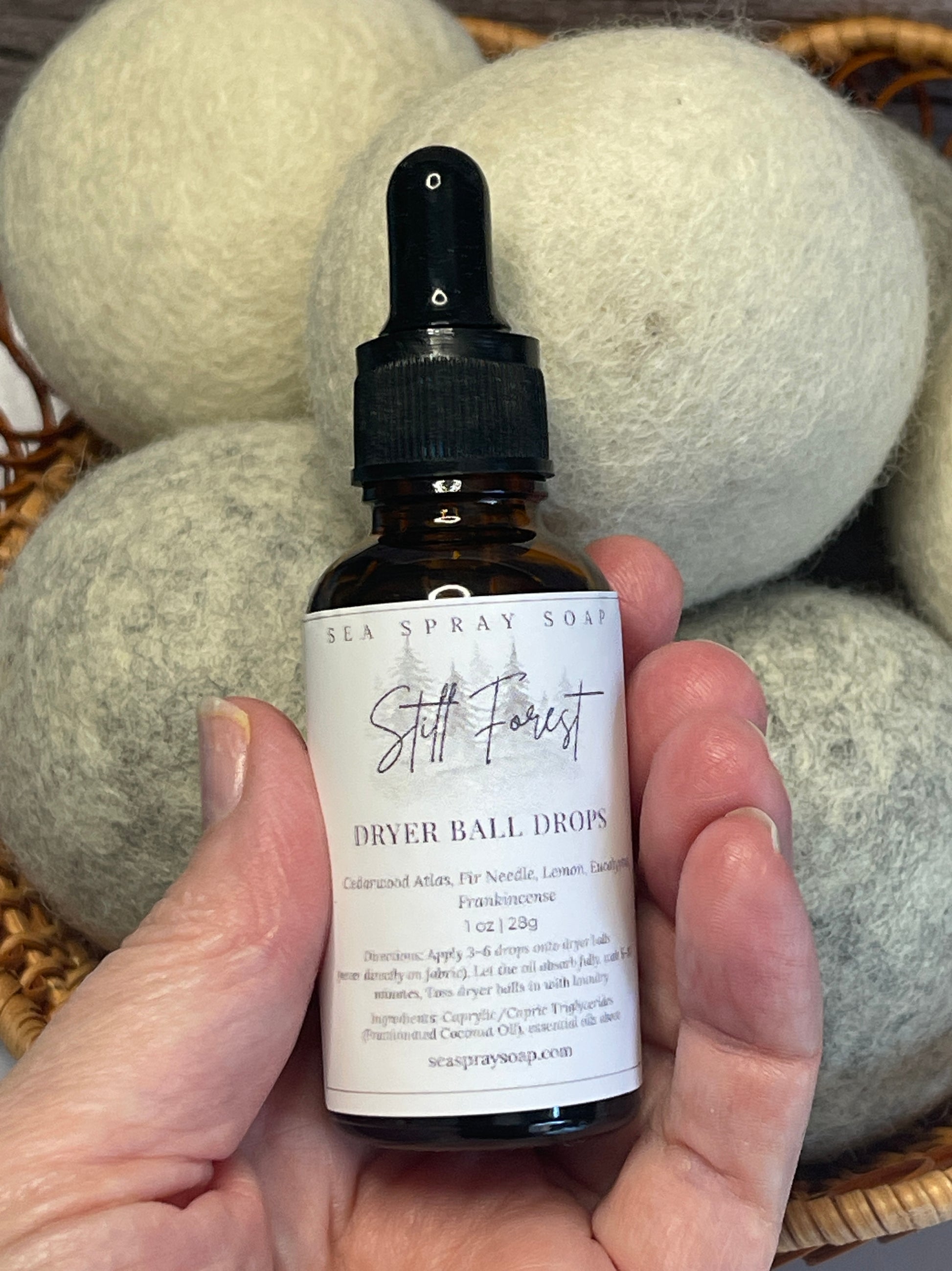 Hand holding a bottle labeled 'Dryer Ball Drying' over dryer balls.