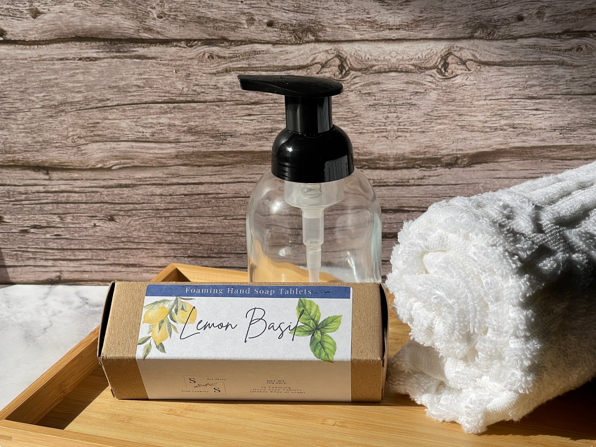 Foaming hand soap with pump and packaging on a wooden tray with a towel in the background.