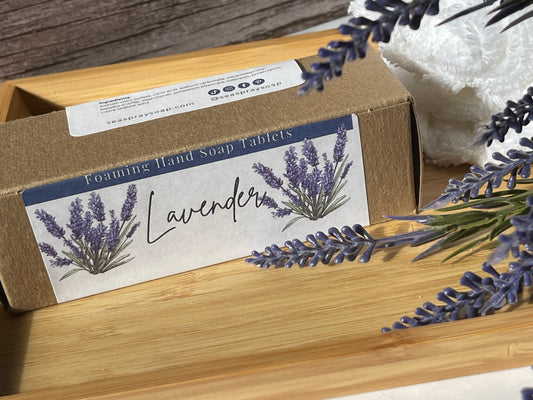 Box of lavender foaming hand soap tablets with lavender flowers on a wooden surface.