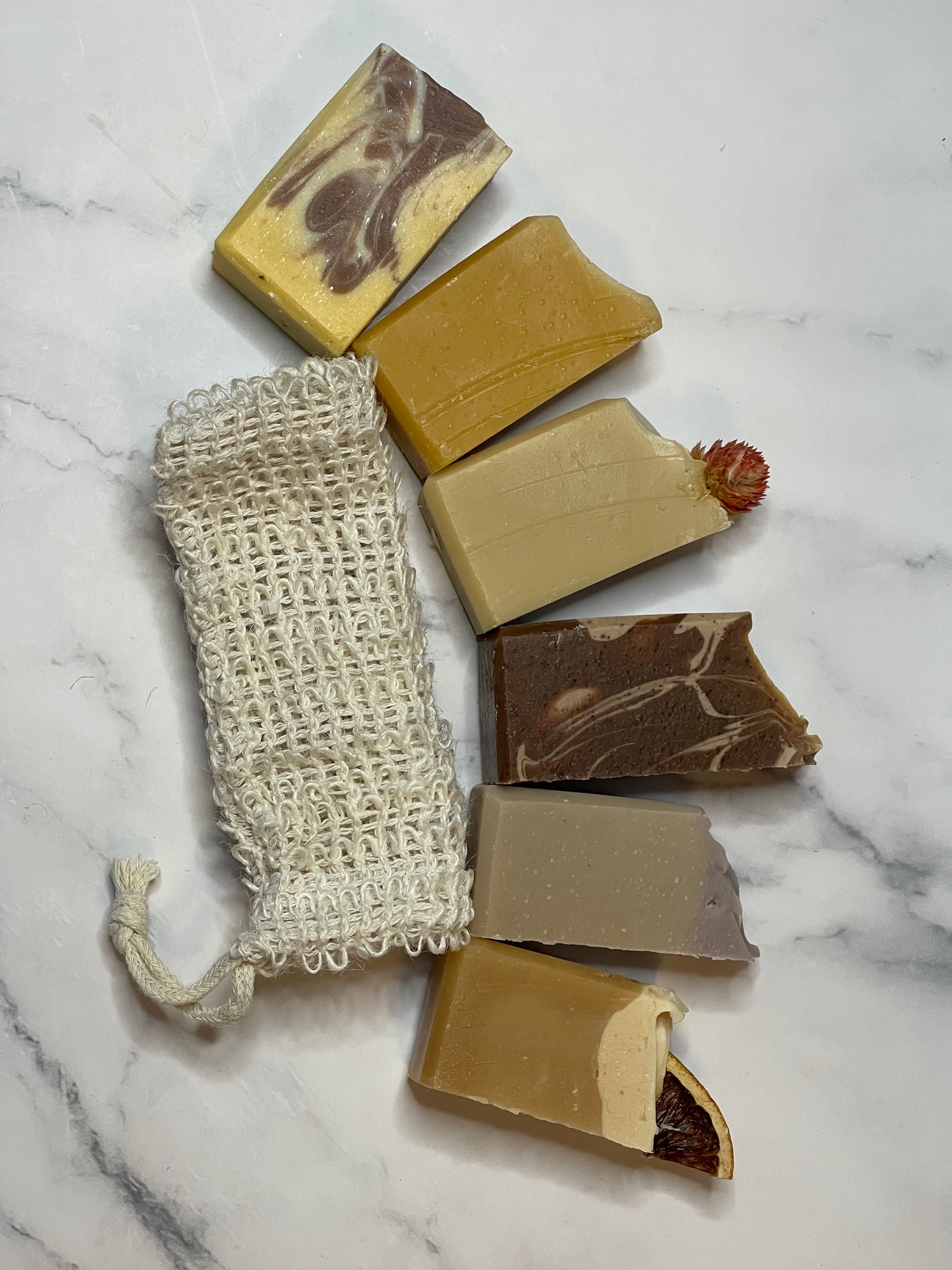 Assorted bars of soap and a natural soap bag on a marble surface