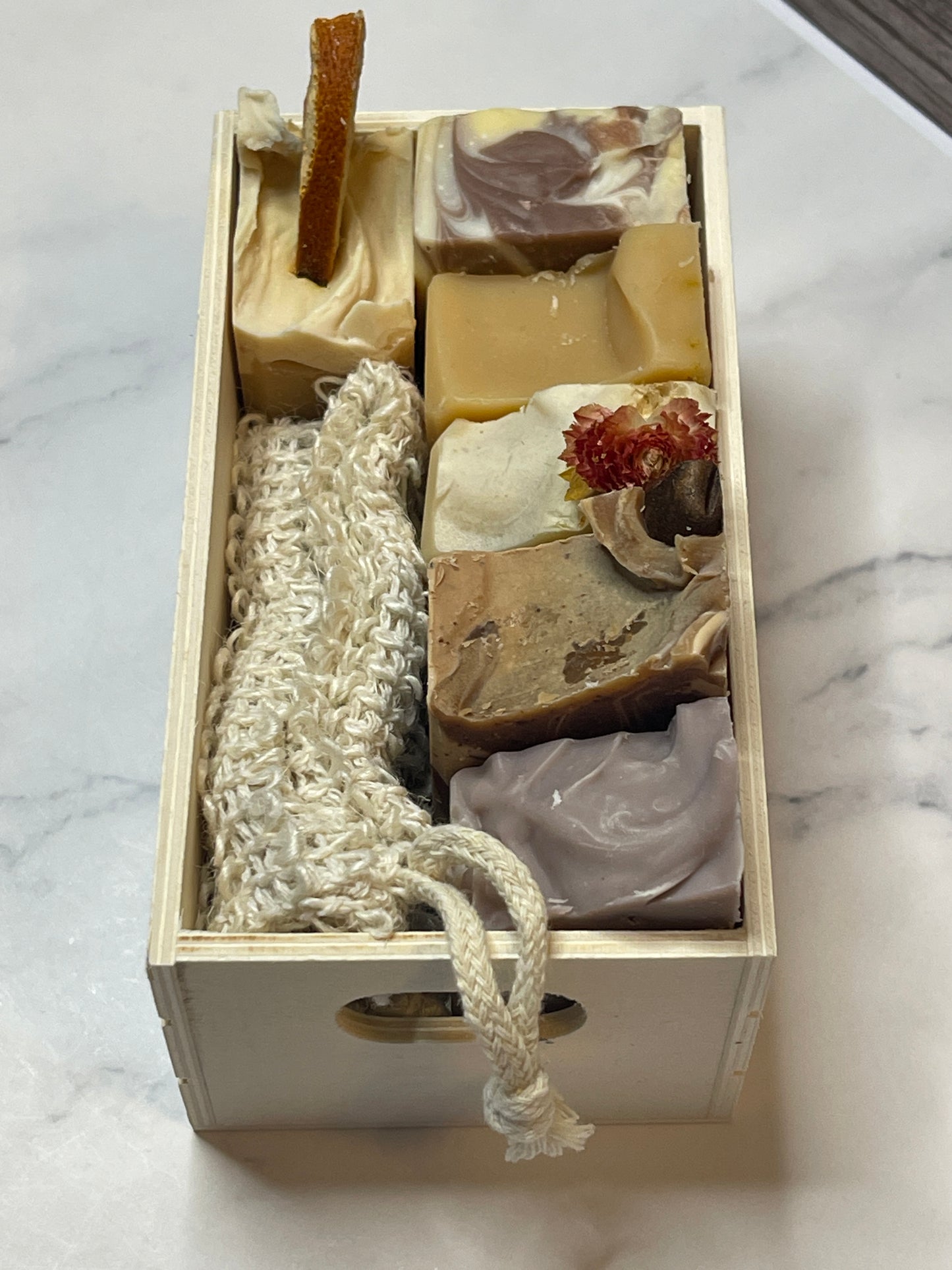Wooden box with various soaps and a loofah on a marble surface