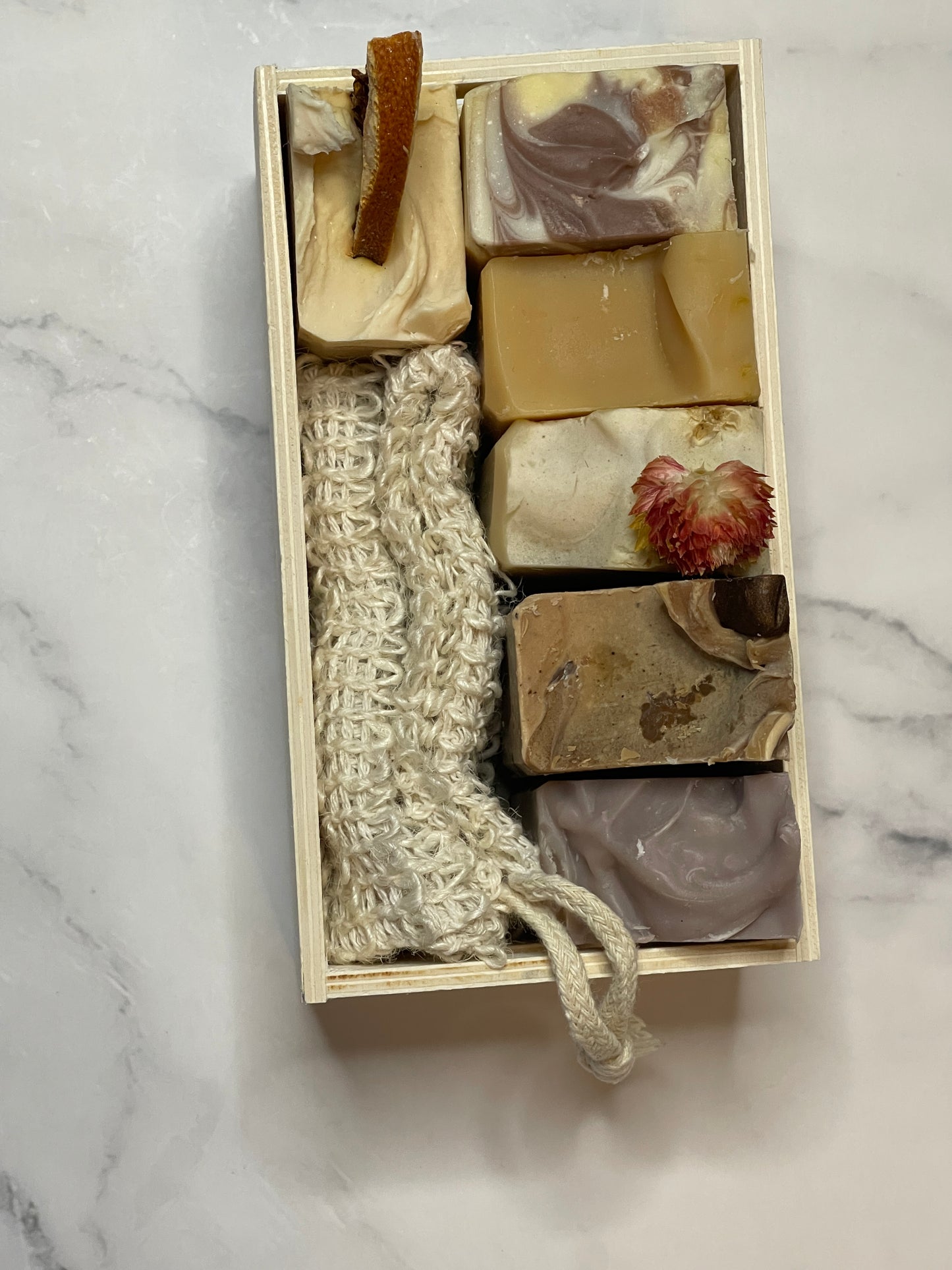 Set of soaps and a loofah in a wooden box on a marble surface