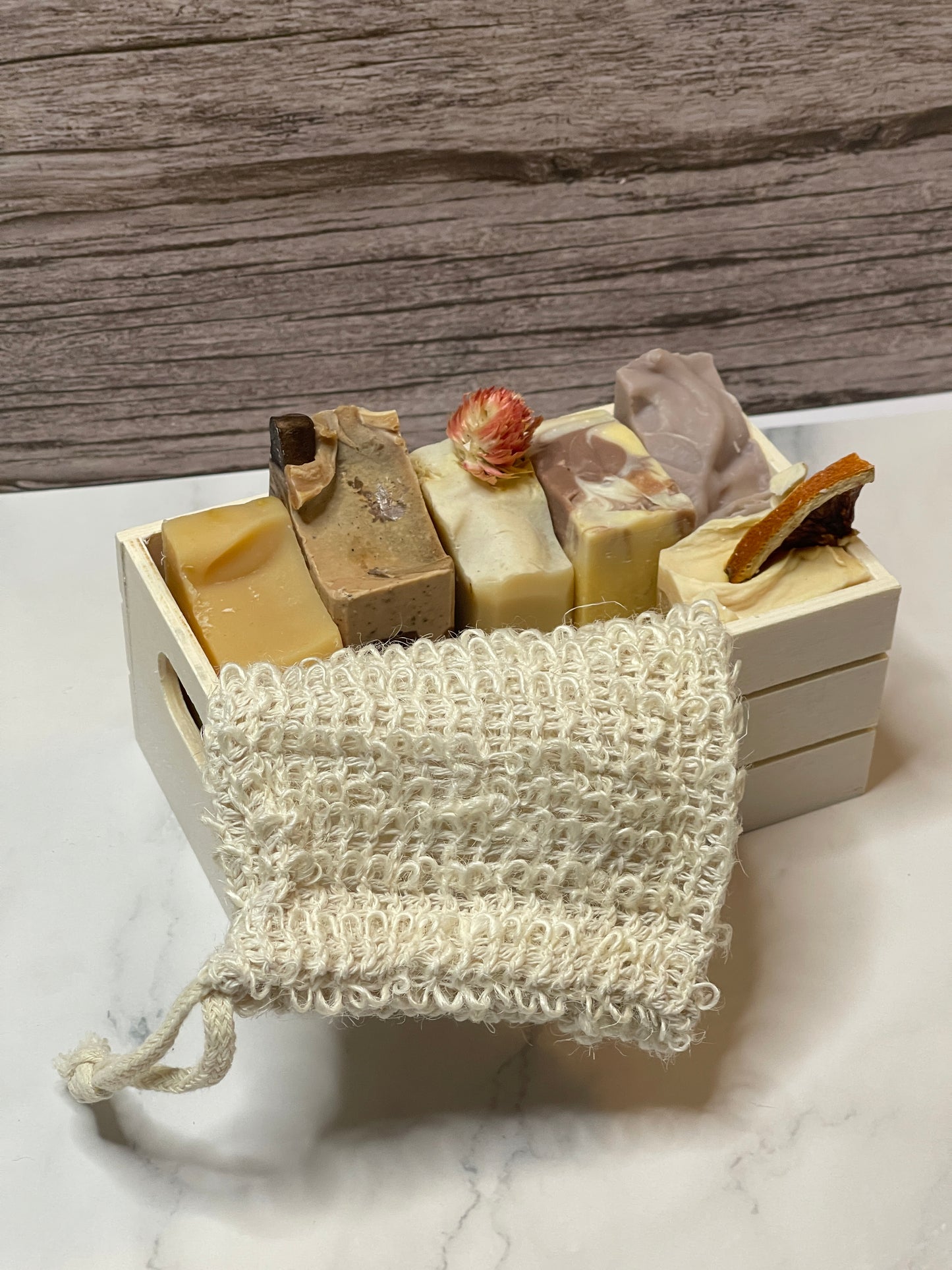 Set of handmade soap bars on a wooden block with a natural fiber soap saver on a marble surface.