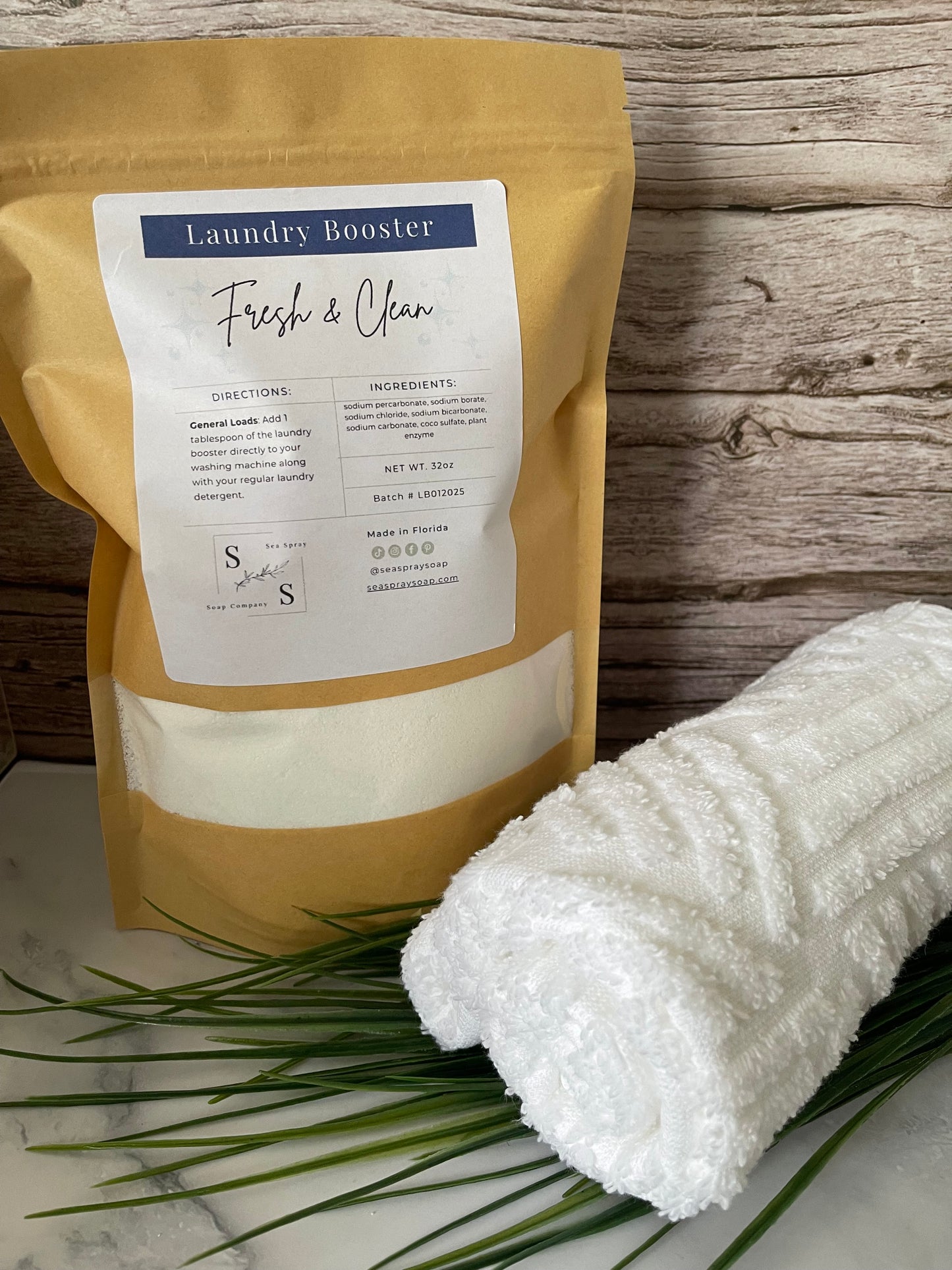 Laundry booster package with a white towel and plant on a wooden surface