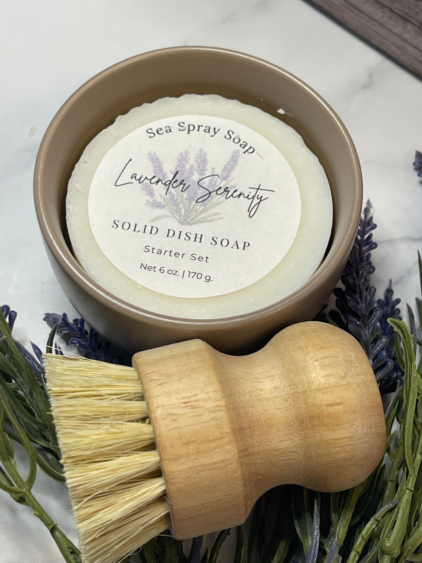 Solid dish soap bar with a wooden brush and lavender flowers on a marble surface