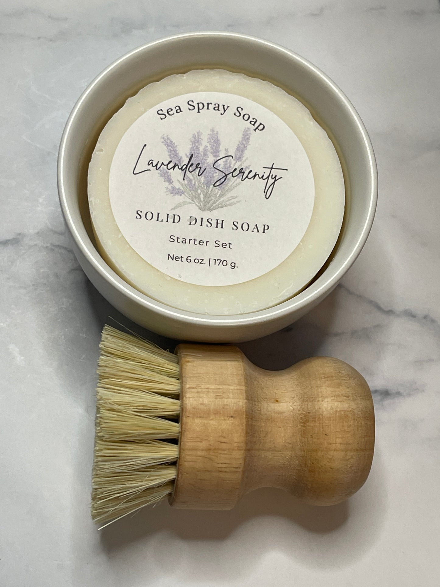 Solid dish soap in a container with a wooden brush on a marble surface