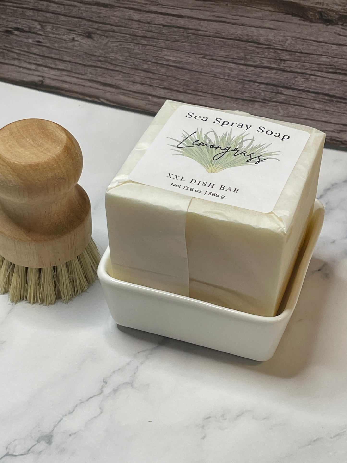 Bar of soap in a white container with a wooden brush on a marble surface