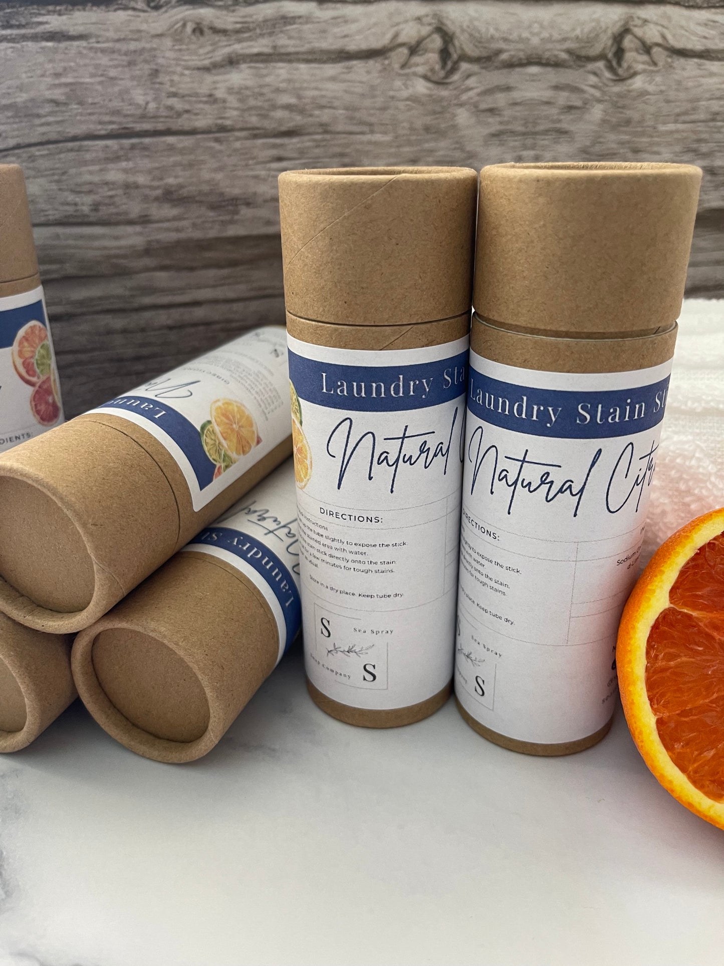 Rolls of laundry stain remover on a wooden and marble surface with an orange slice.