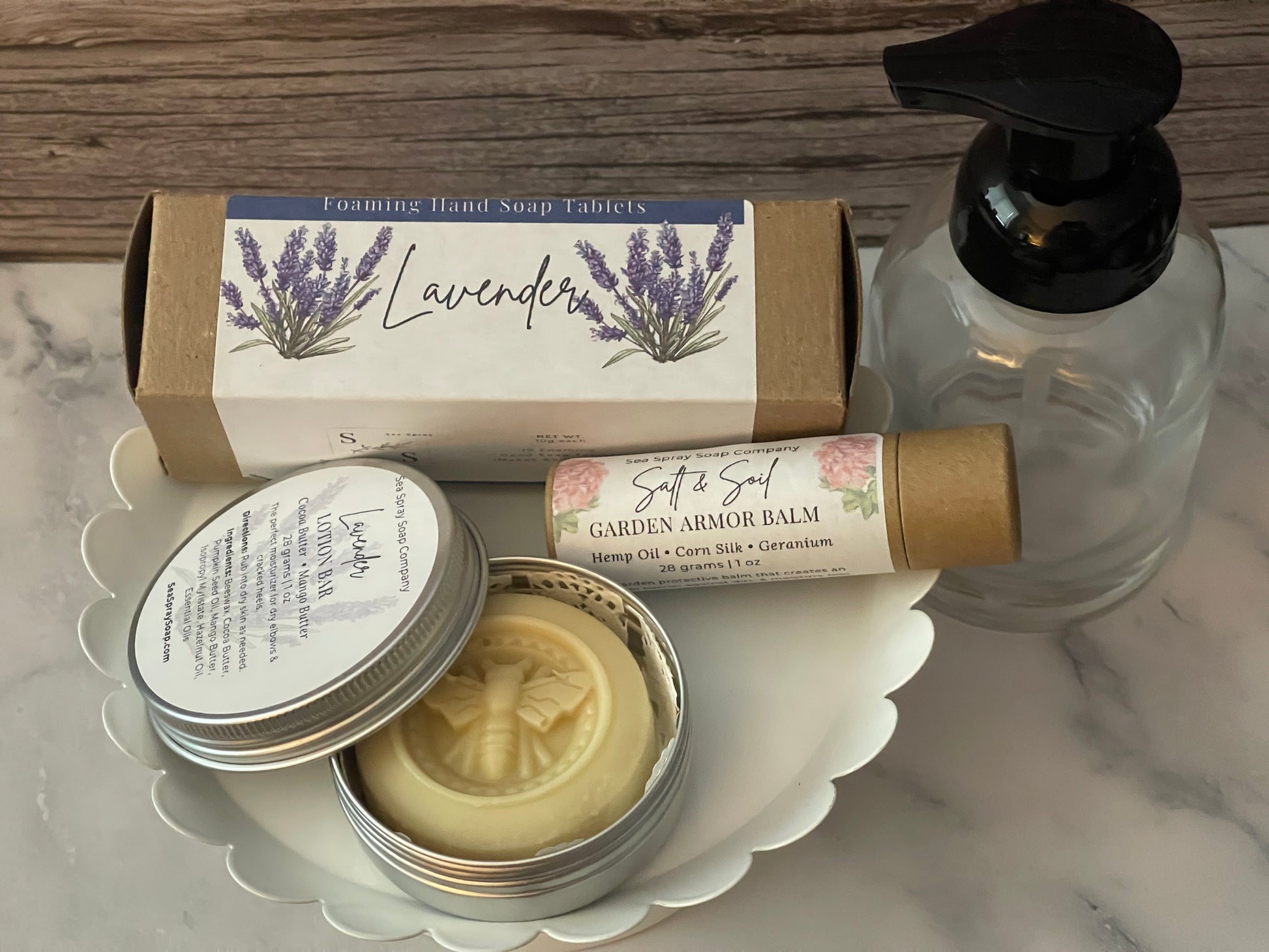 Collection of natural skincare products including a tin, bottle, and bar on a marble surface.