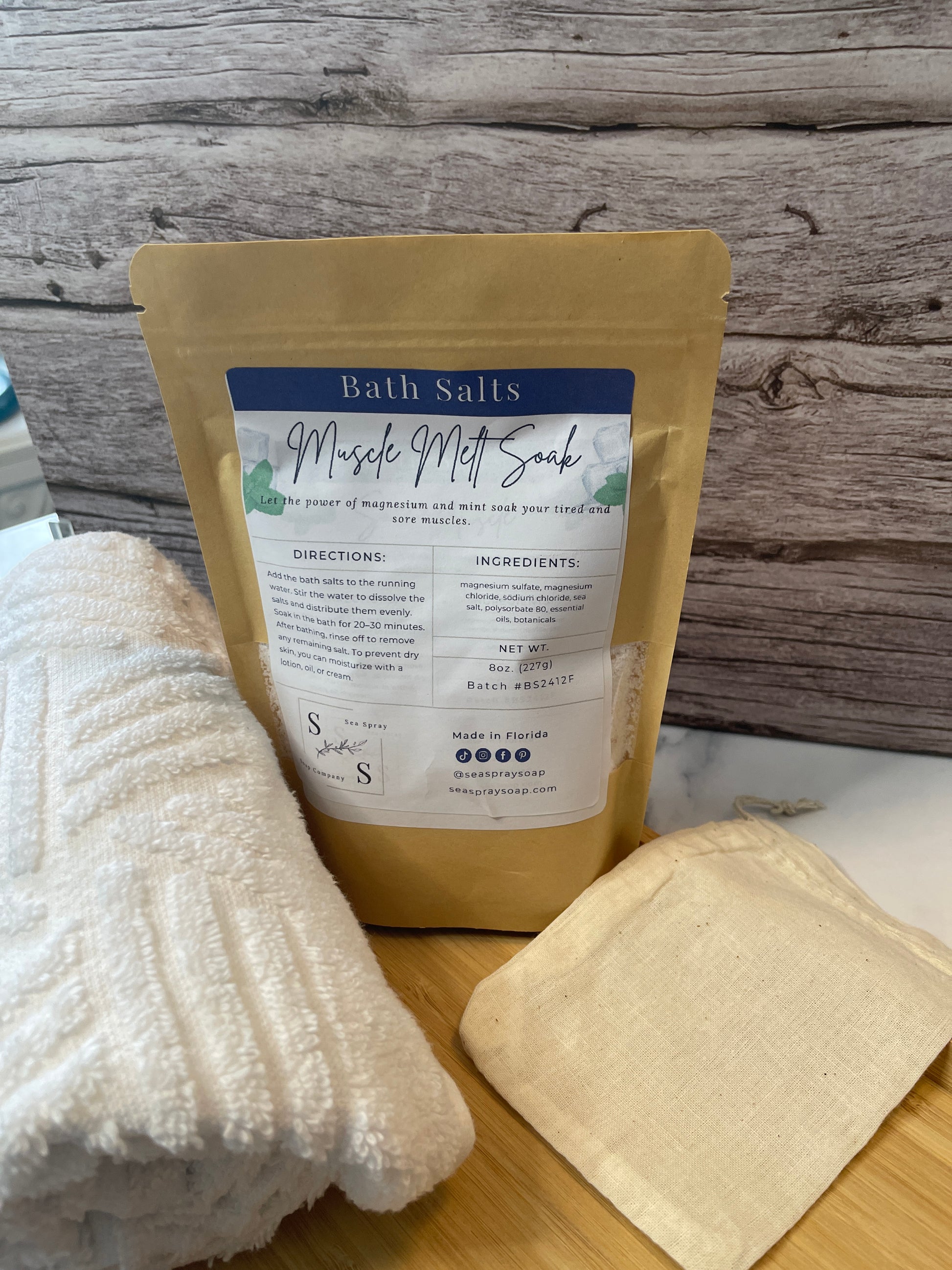 Kraft paper package with a label on a wooden surface next to a bar of soap and a white cloth.