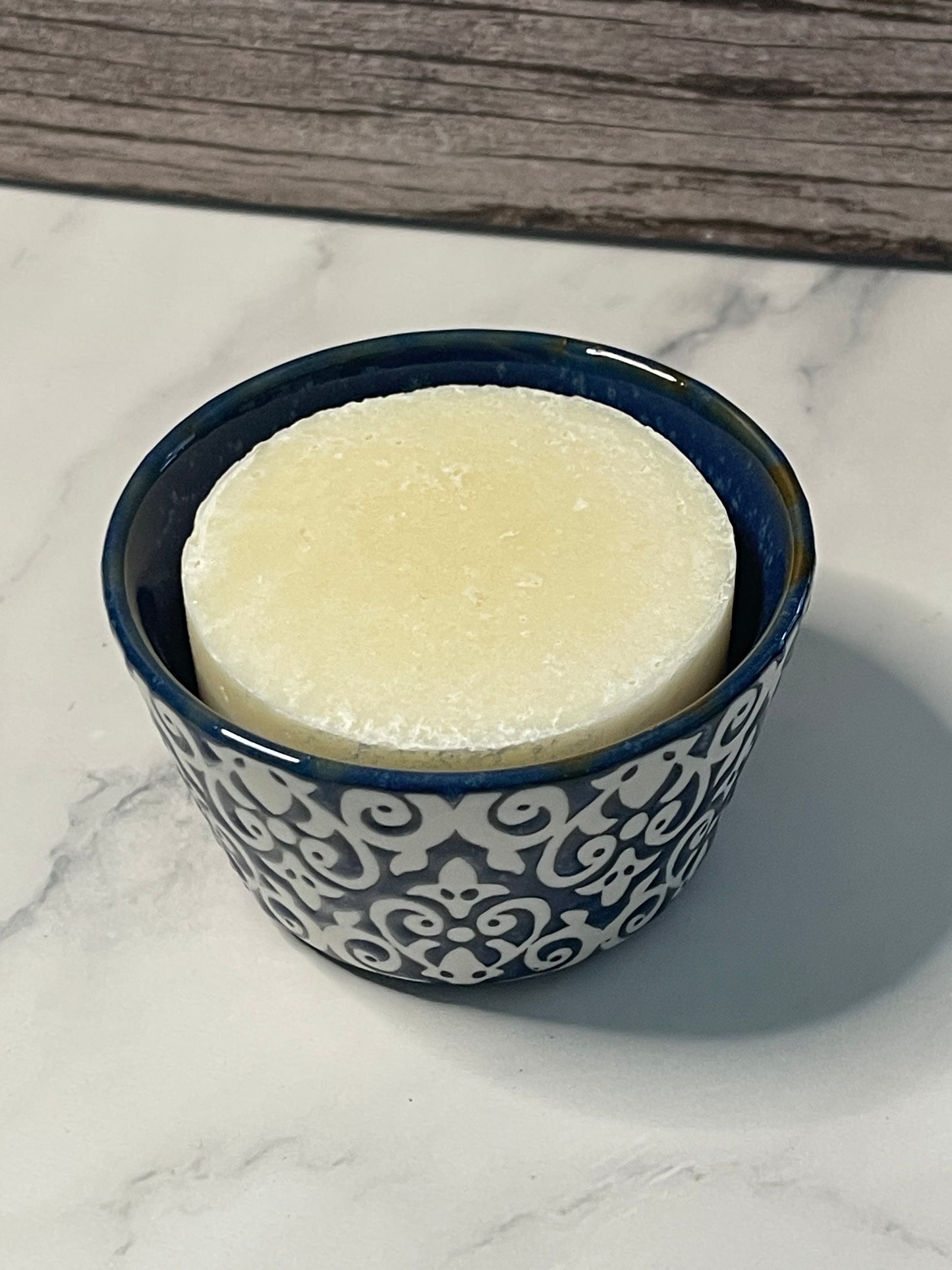 Blue ceramic container with decorative patterns holding a white bar of soap on a marble surface.