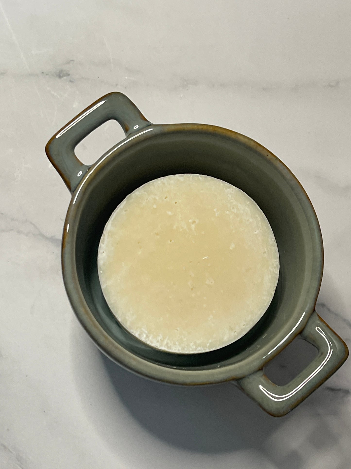Green ceramic pot with solid dish soap on a marble surface