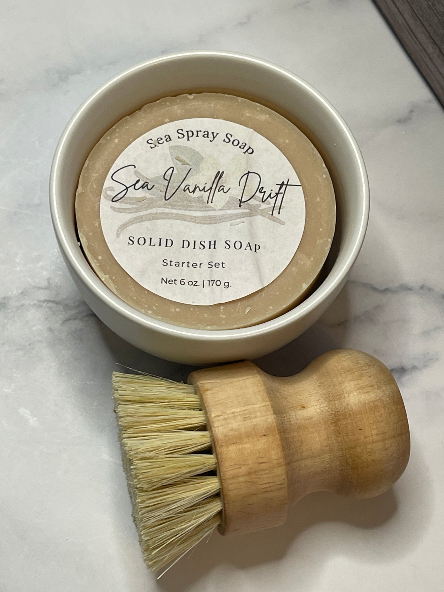 Solid dish soap in a container with a wooden brush on a marble surface