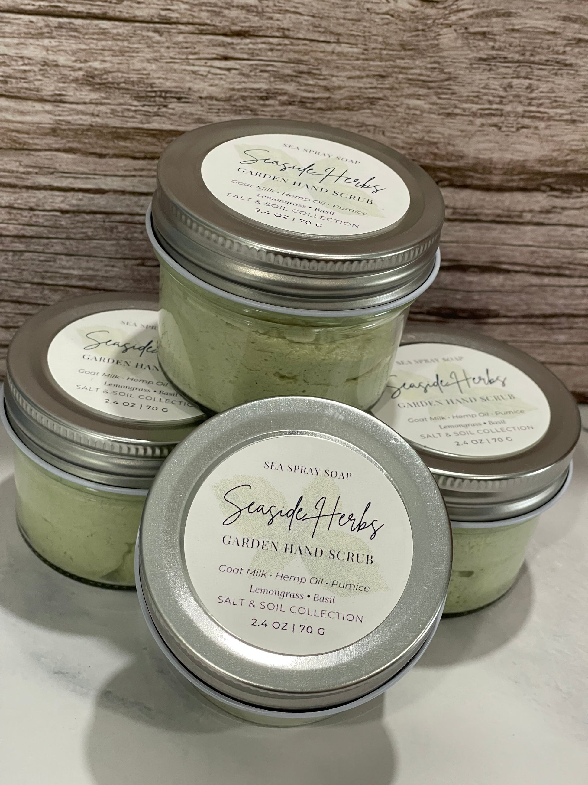 Four jars of handmade soap with visible branding on a wooden surface.