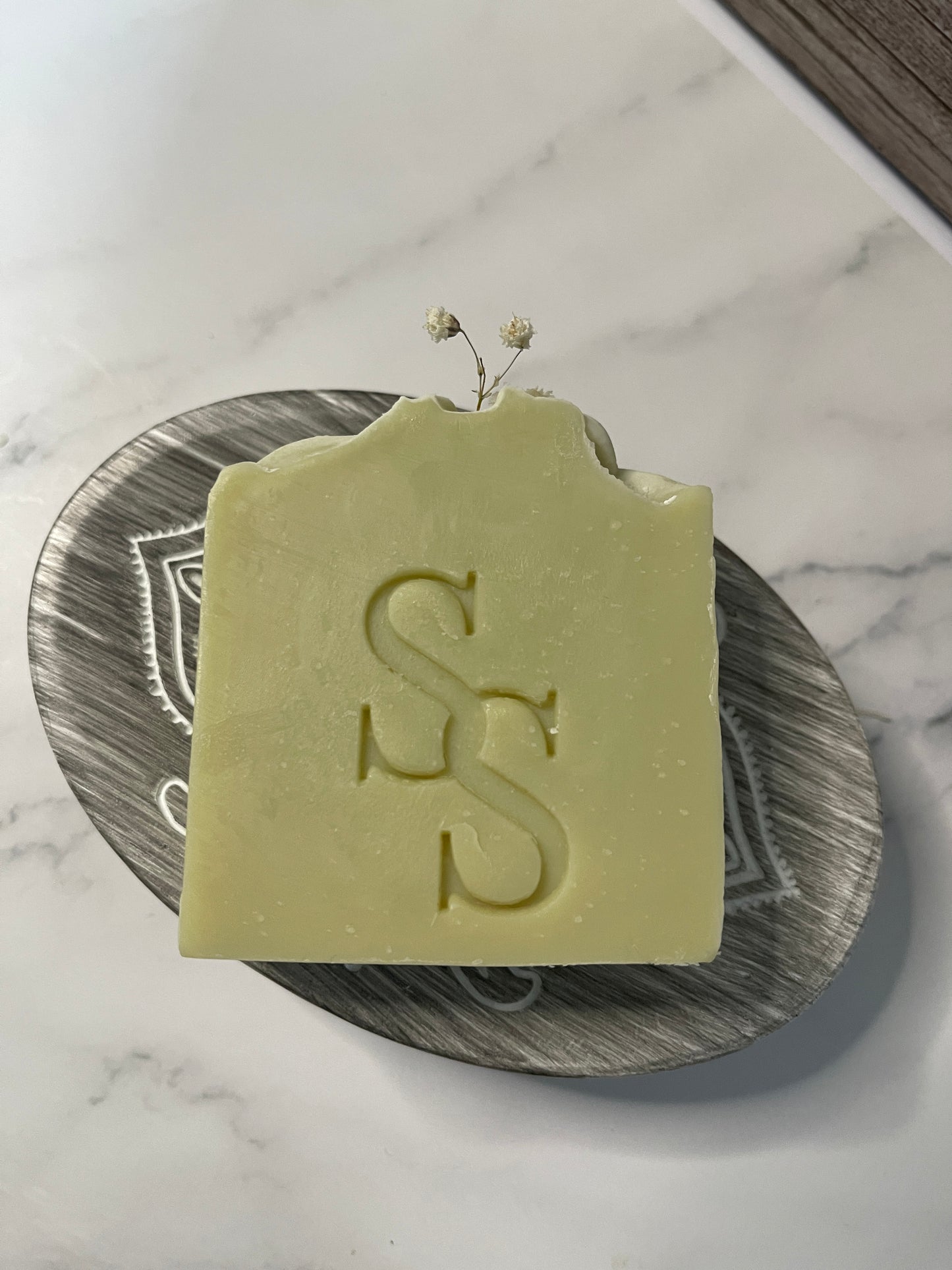 Green soap bar with a logo on a metallic dish against a marble background