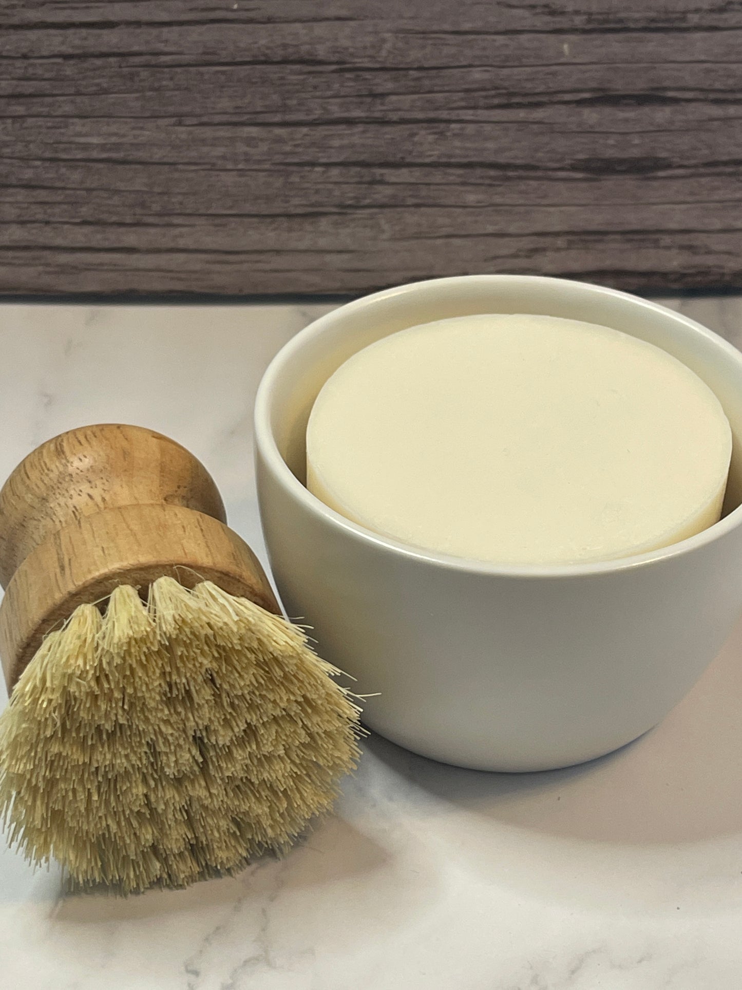 Shaving brush and cream on a marble surface with wooden background