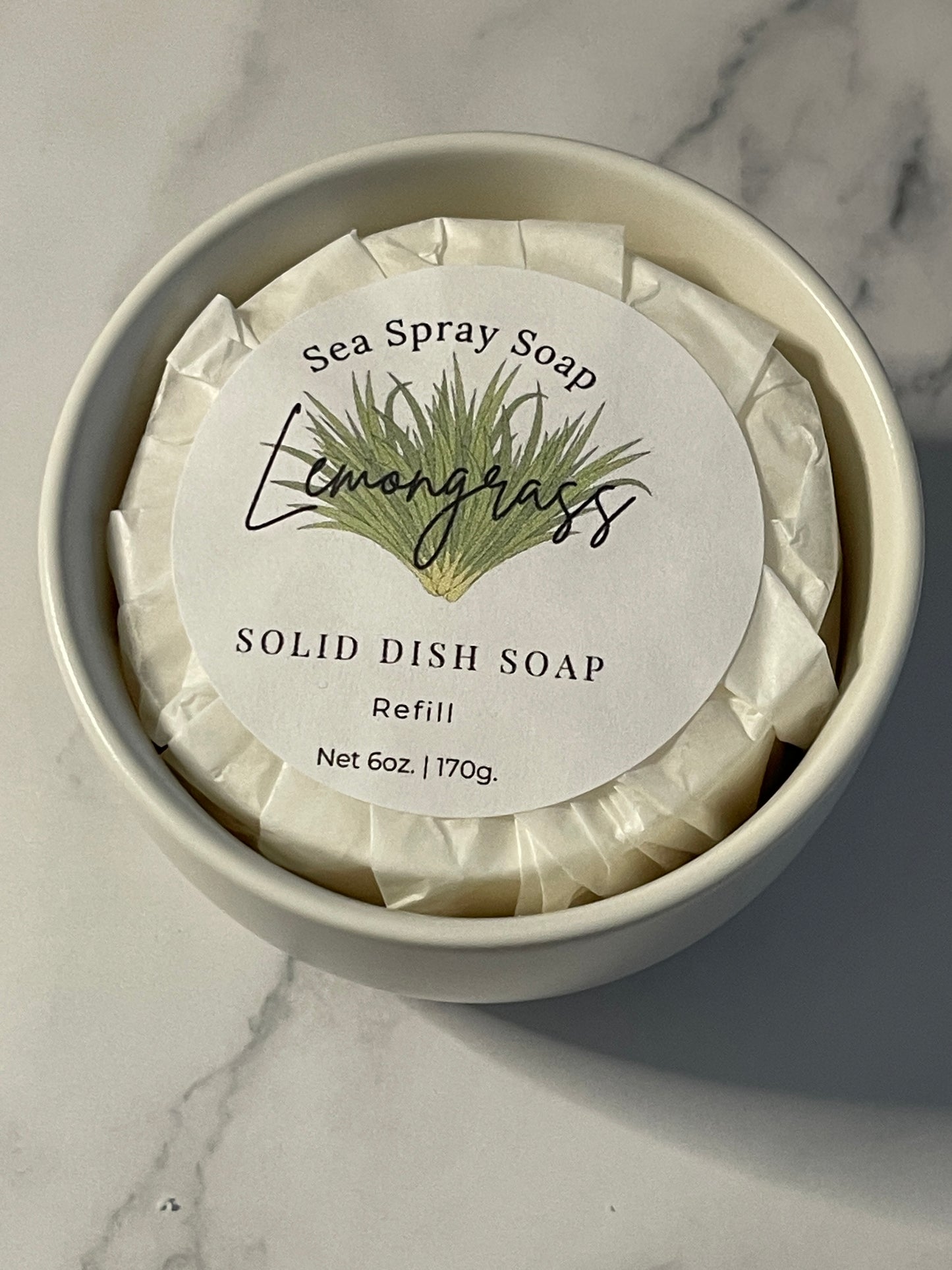 Solid dish soap bar in a container with a label on a marble surface