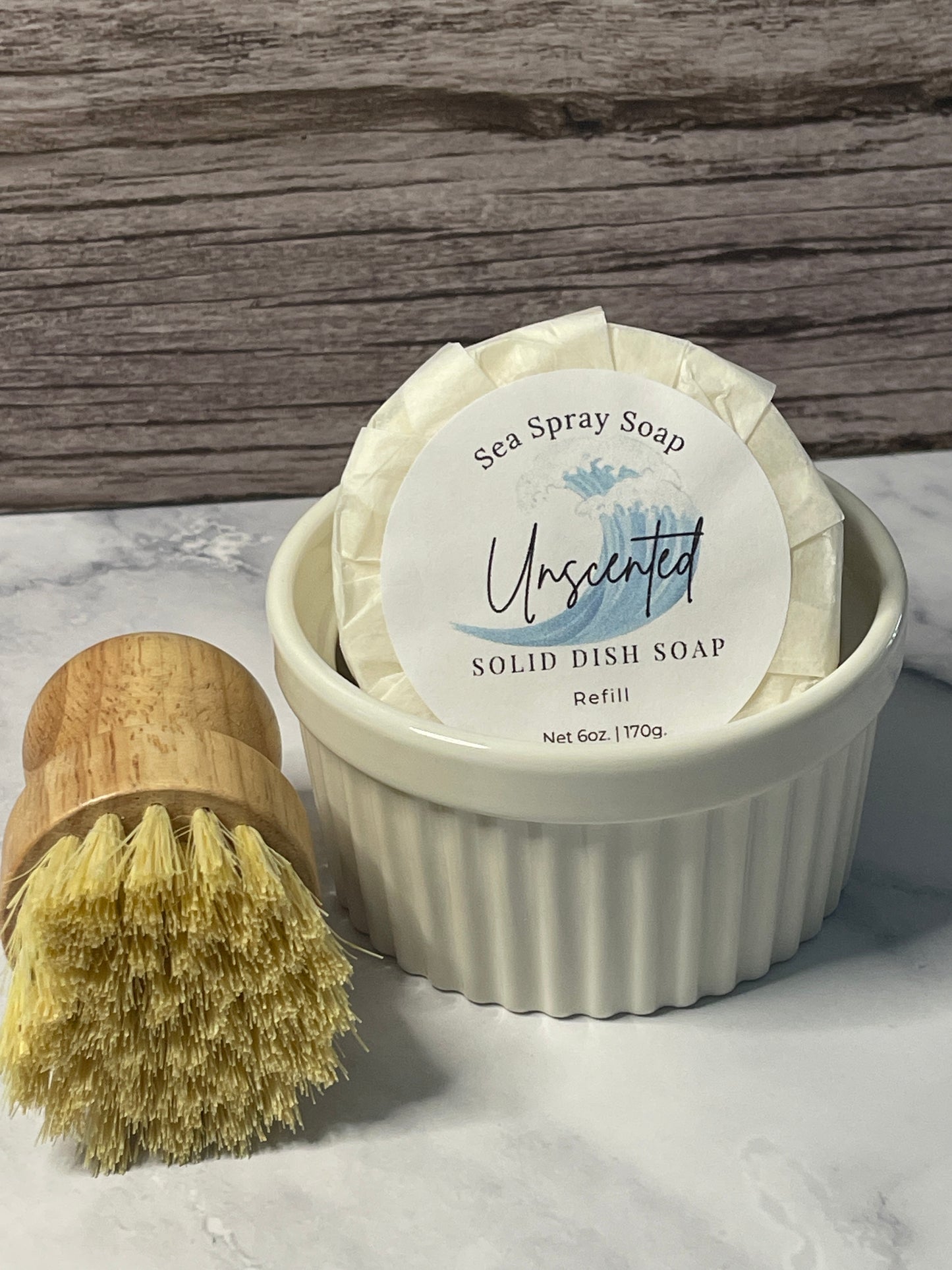 Solid dish soap in a white container with a brush on a marble surface