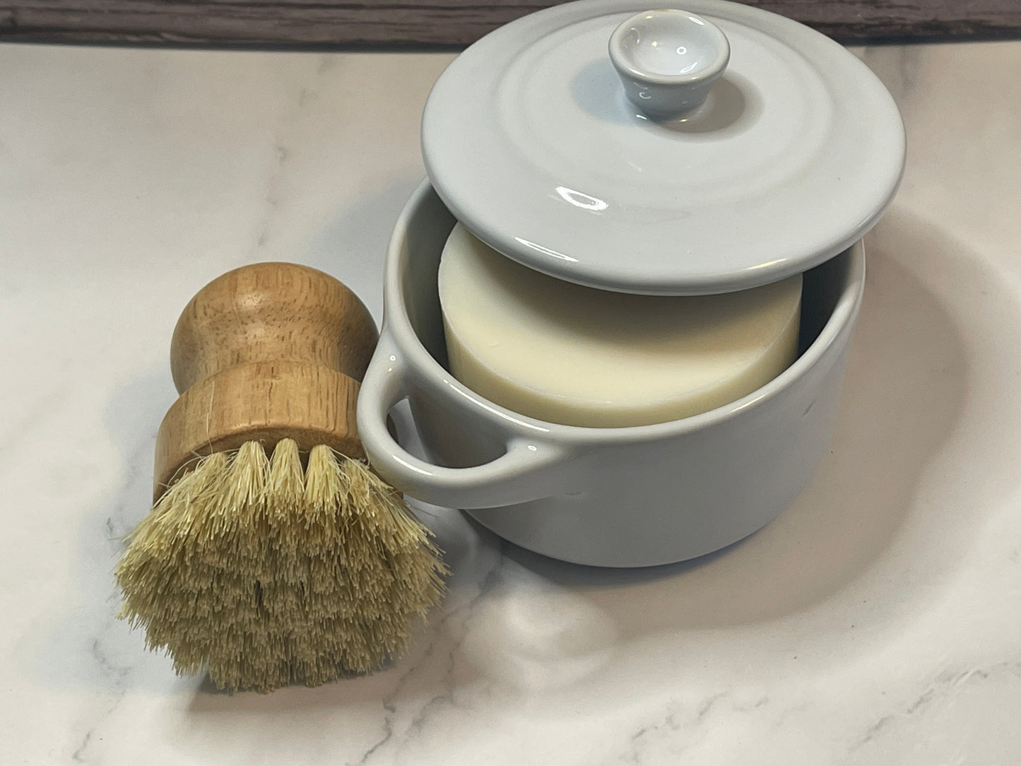 White ceramic mug with wooden brush on a marble surface