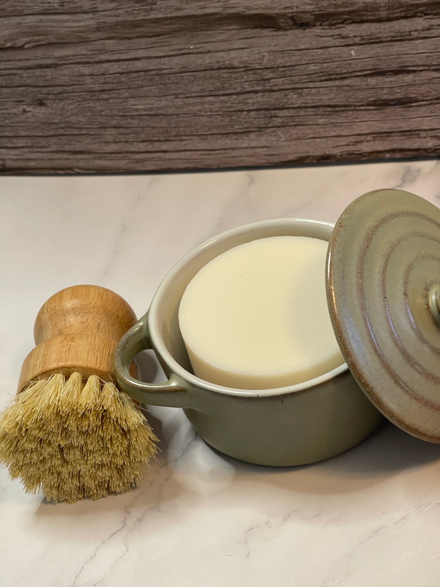Green ceramic soap dish with a bar of soap and a wooden brush on a marble surface.