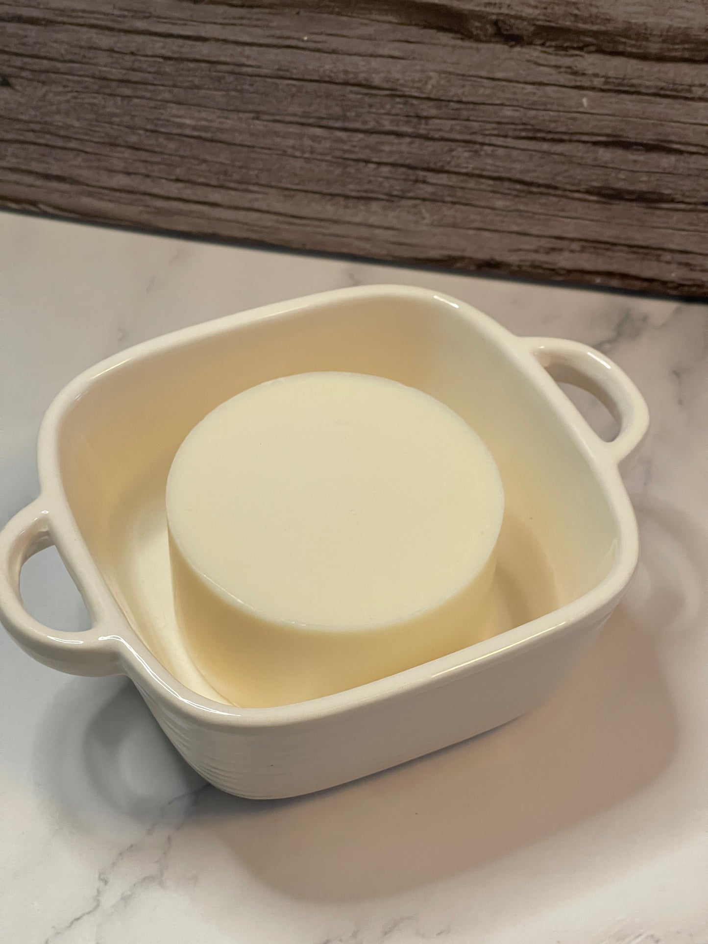 White soap bar in a beige soap dish on a wooden surface