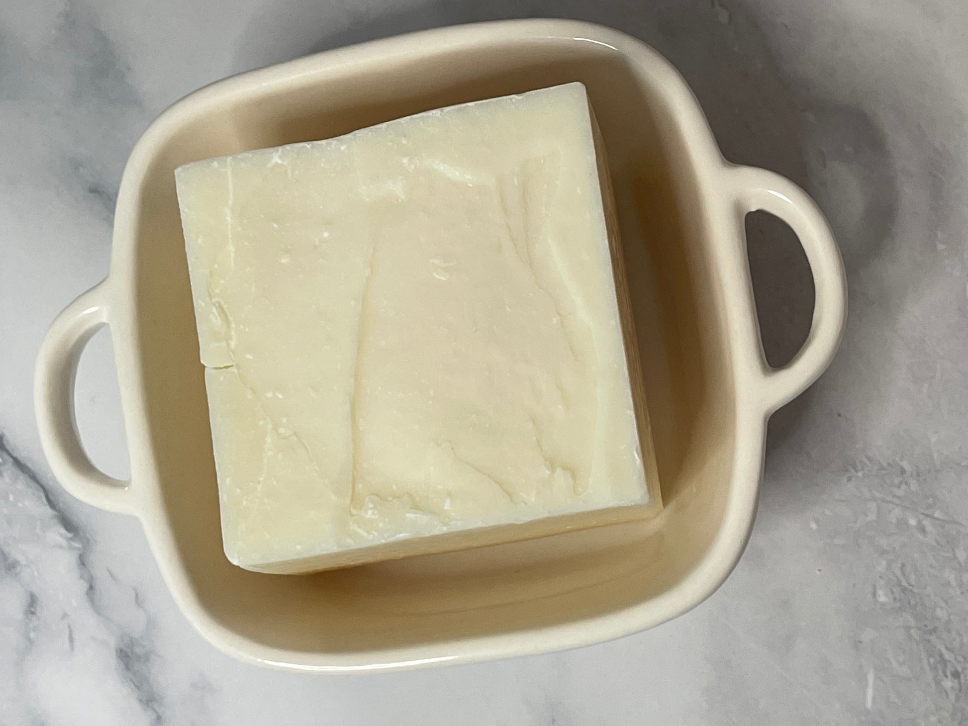 Solid dish soap in a beige dish on a marble surface