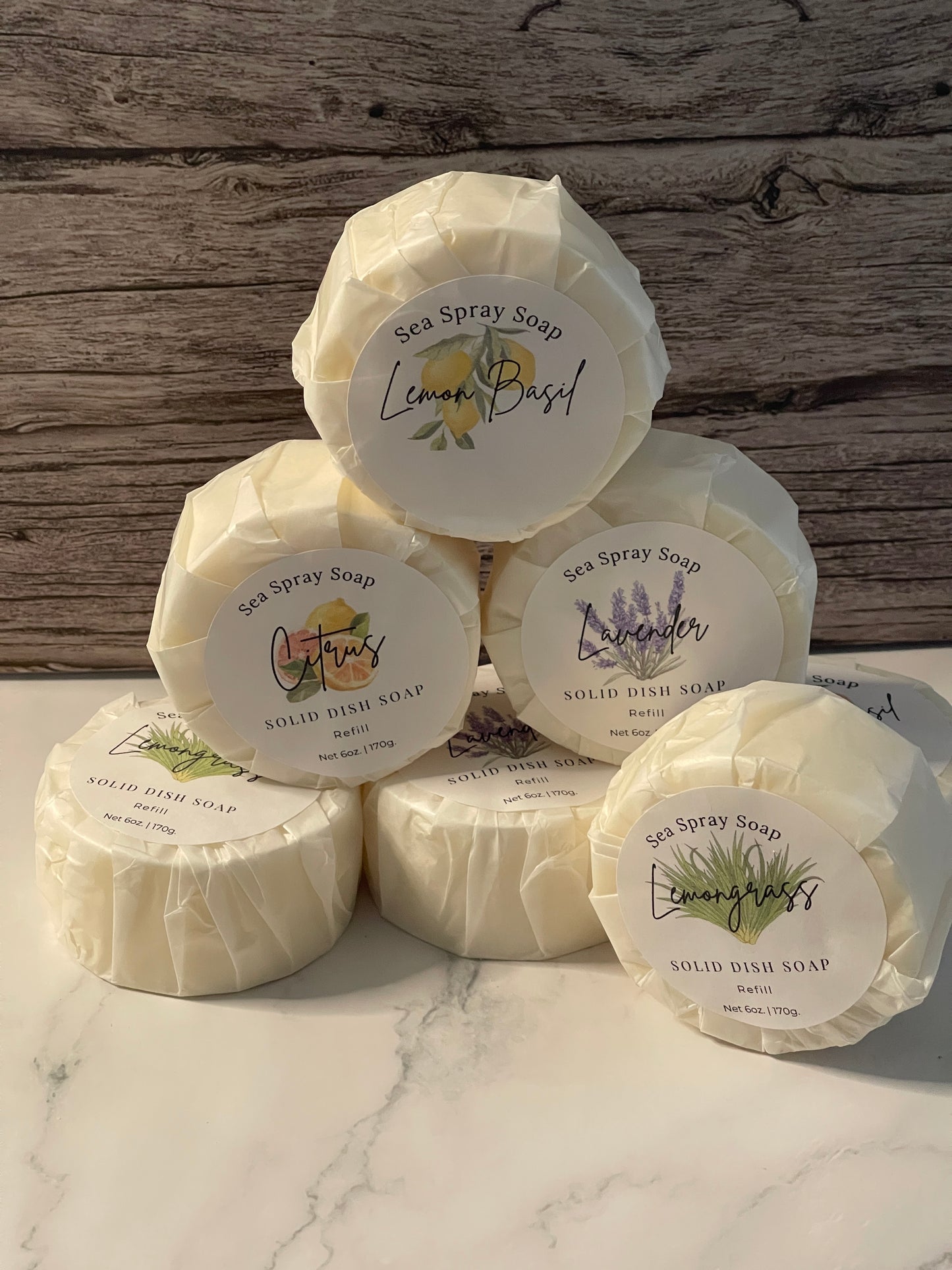 Multiple wrapped soaps with labels on a wooden and marble surface