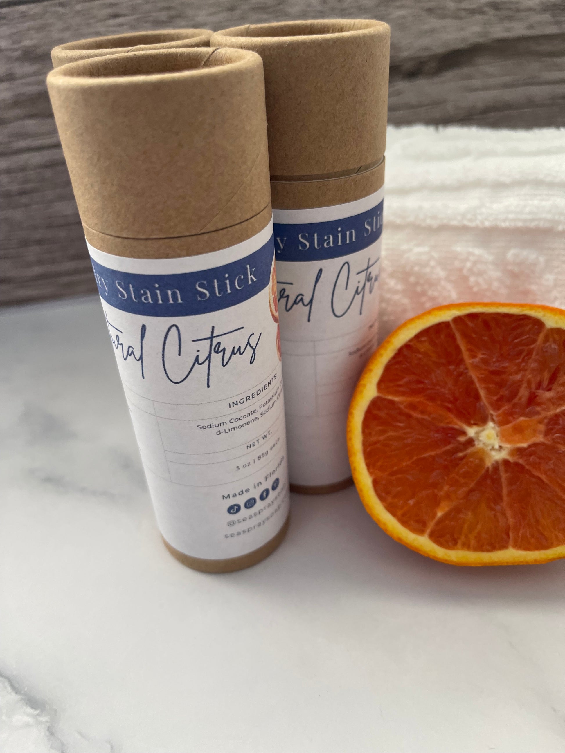 Two cylindrical products with labels next to a halved orange on a white surface.