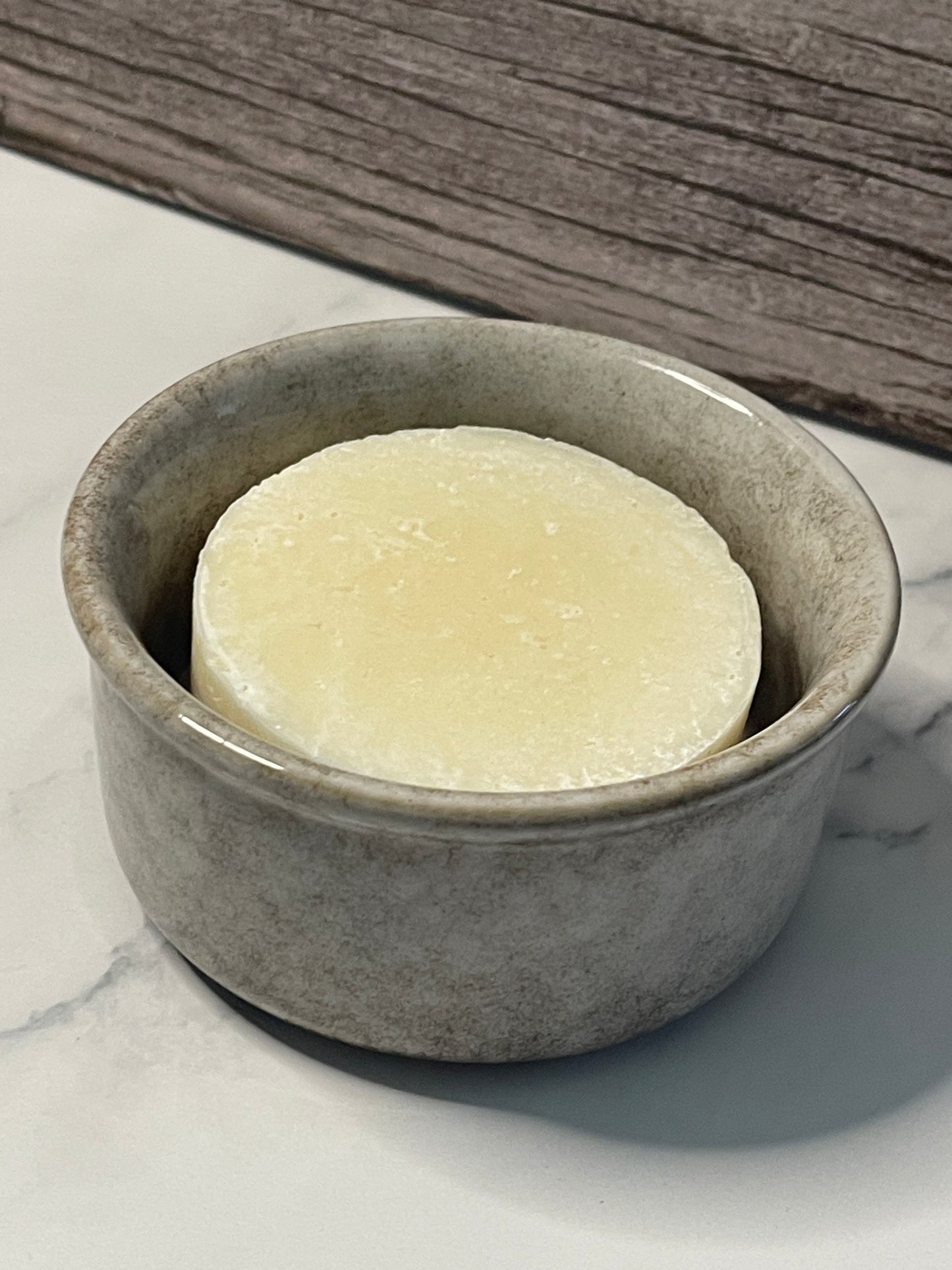 Bar of soap in a tan ceramic dish on a marble surface