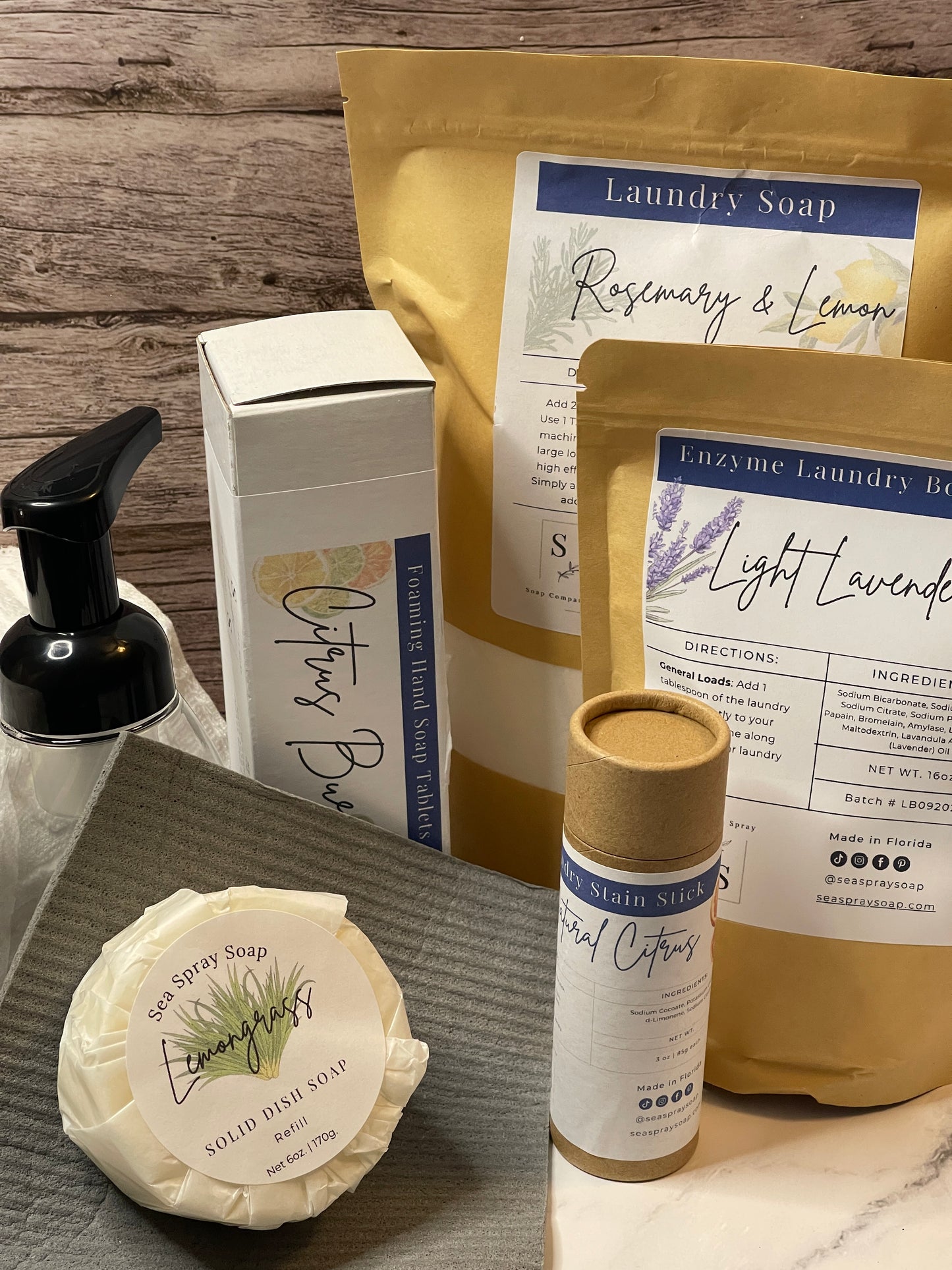 Collection of natural cleaning products including laundry soap, hand soap tablets, and a bar soap on a wooden surface.