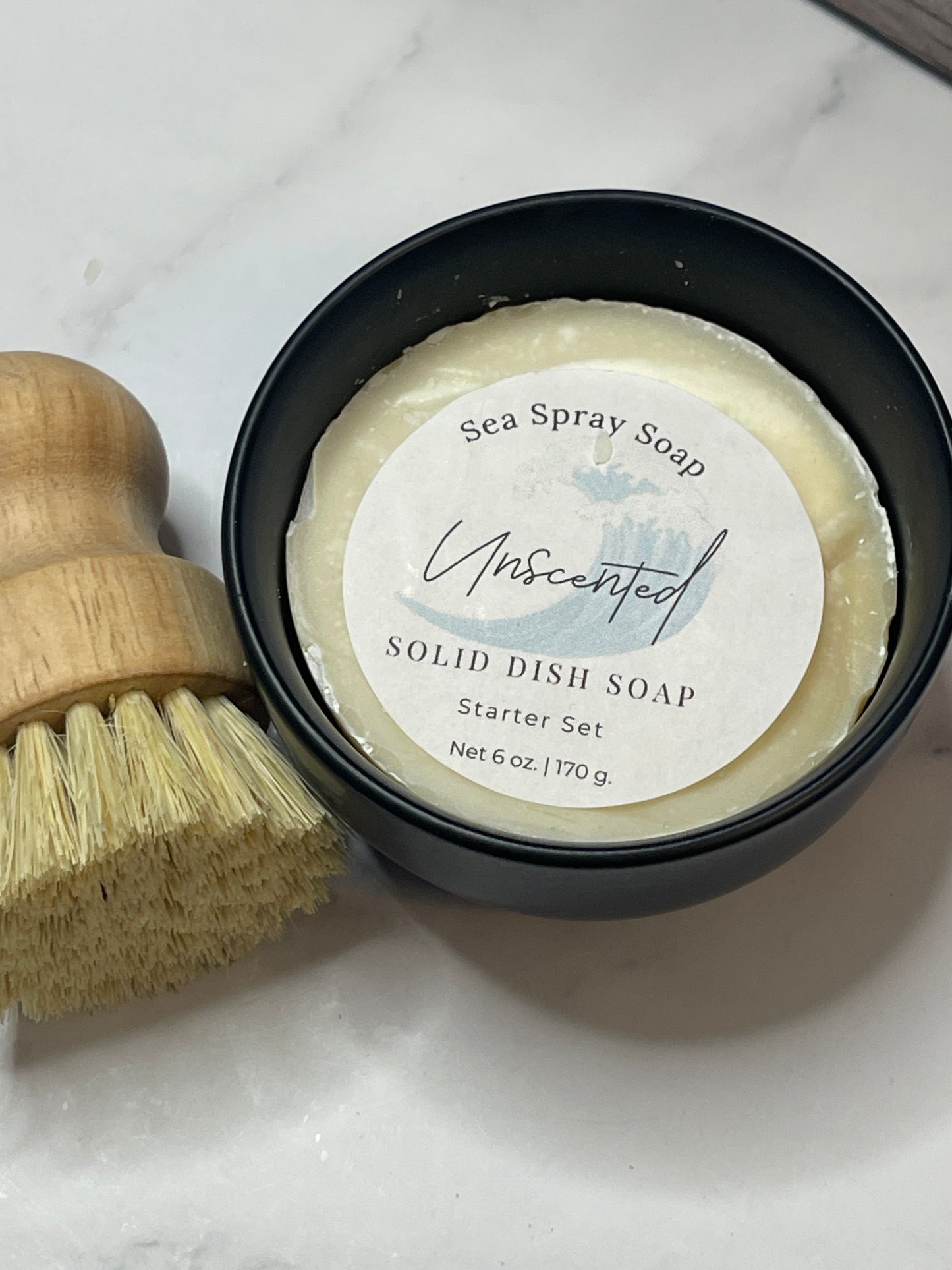 Solid dish soap in a black container with a brush on a marble surface