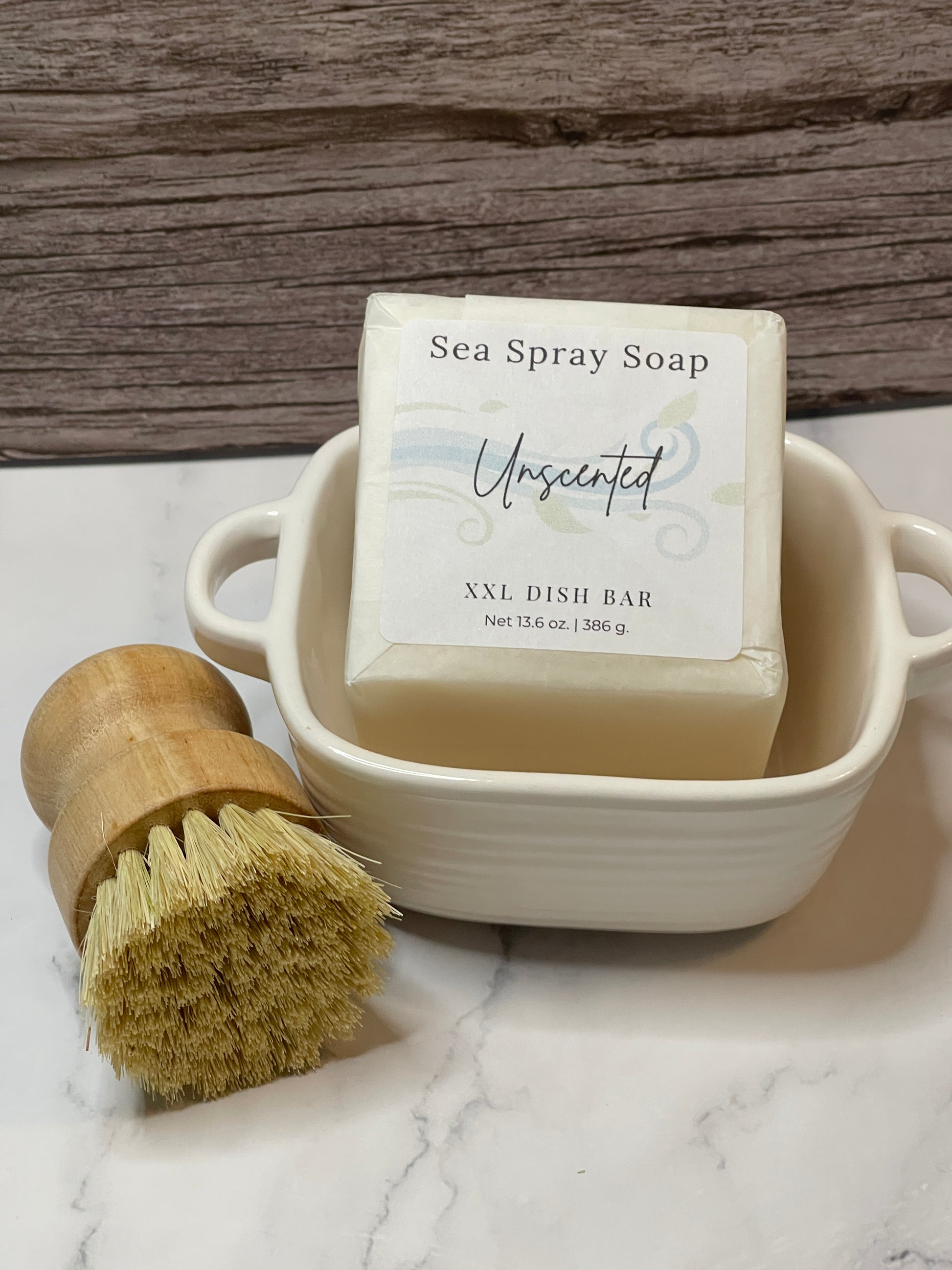 Bar of soap in a ceramic dish with a wooden scrubbing brush on a marble surface.