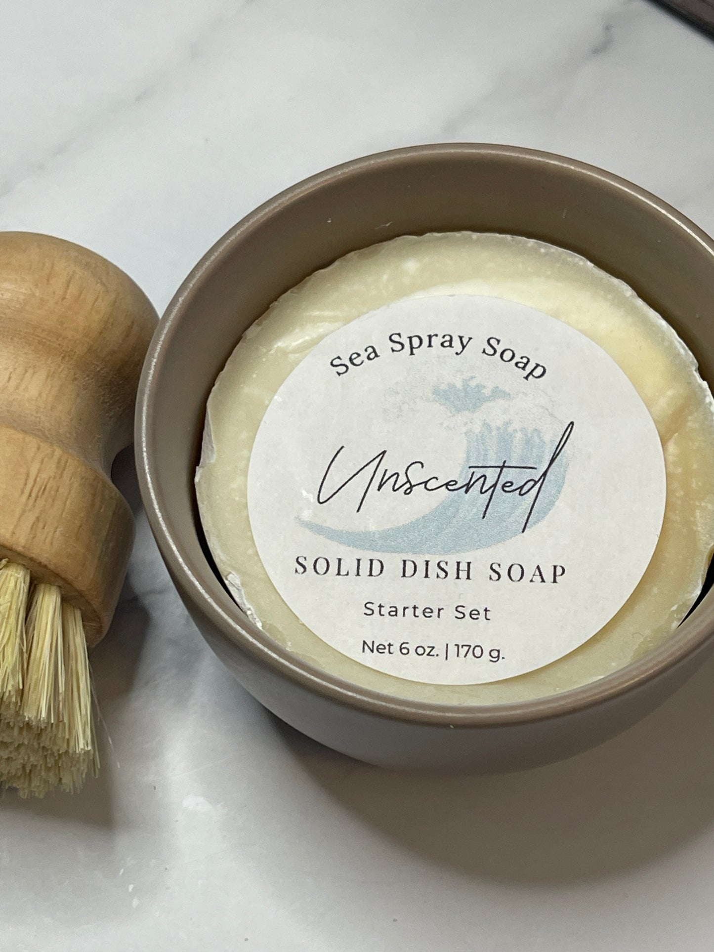 Solid dish soap bar in a container with a wooden brush on a marble surface