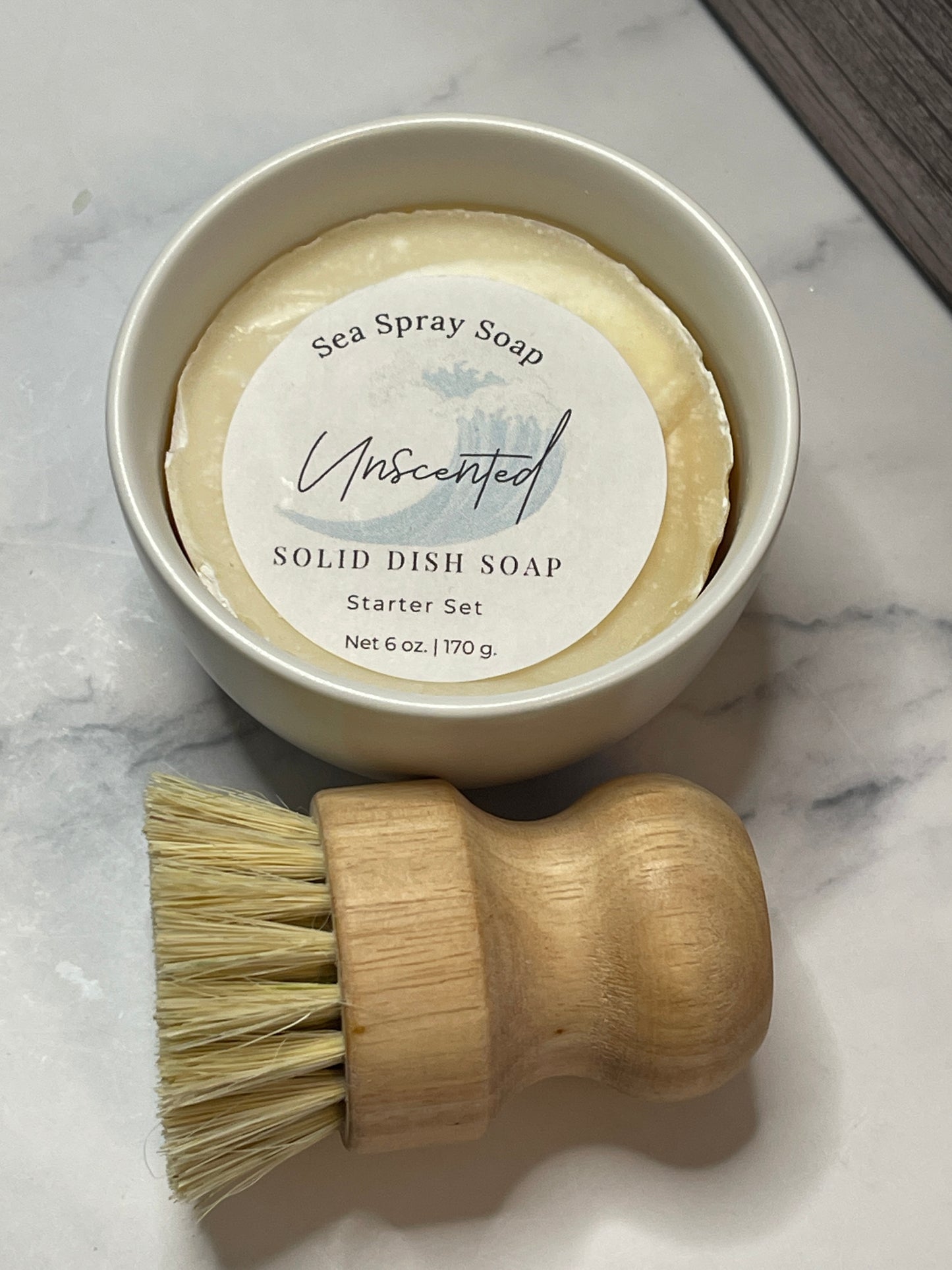 Solid dish soap in a container with a wooden brush on a marble surface