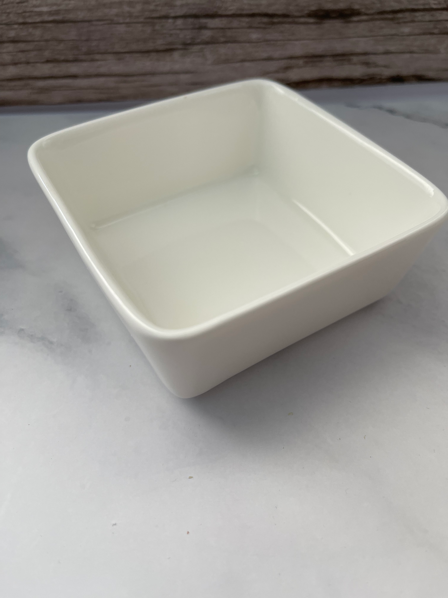 Two large white solid dish soap blocks next to a bamboo dish brush on a marble surface with a wooden wall in the background.