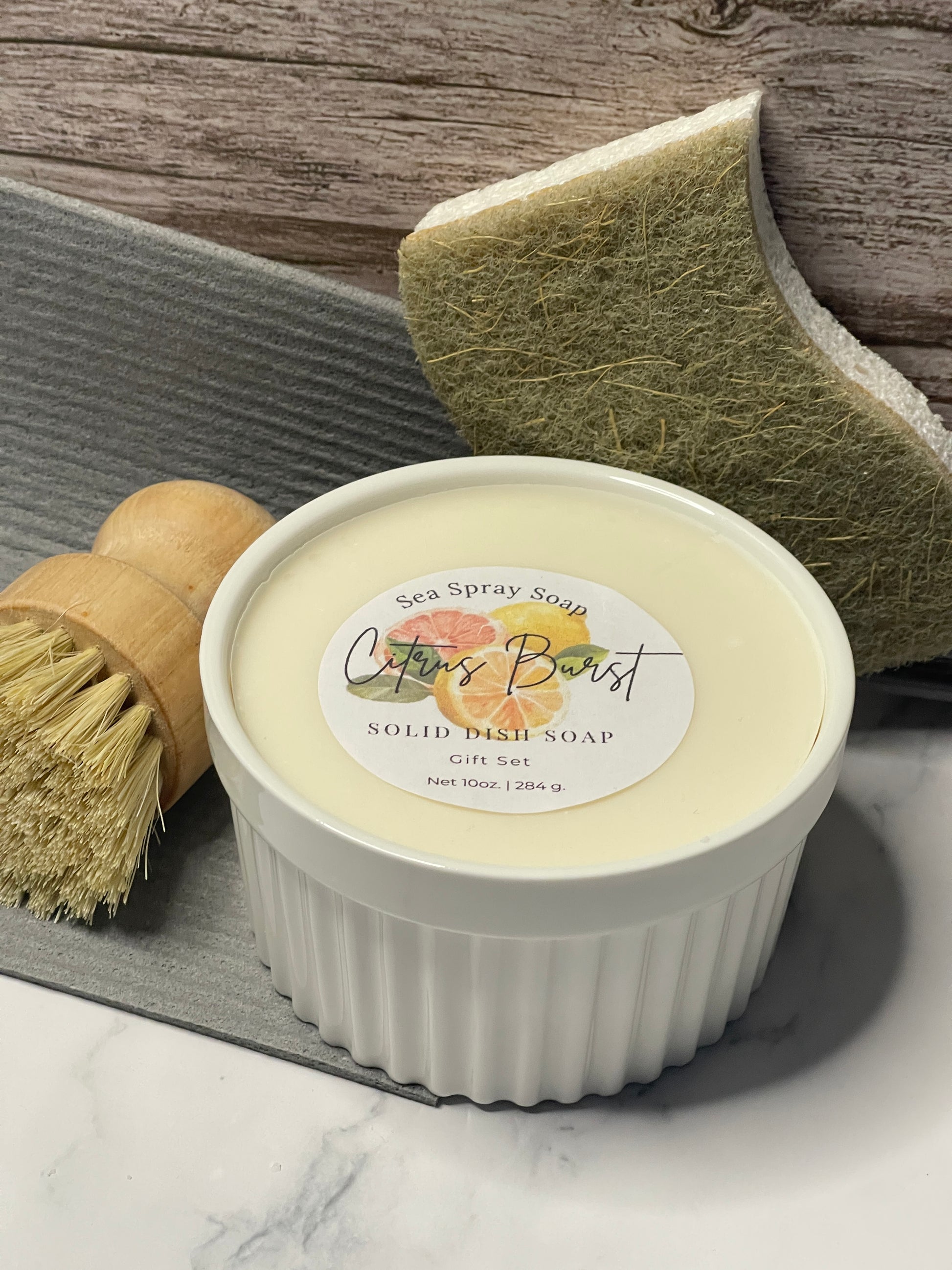 White container with a label, green sponge, and brush on a wooden surface