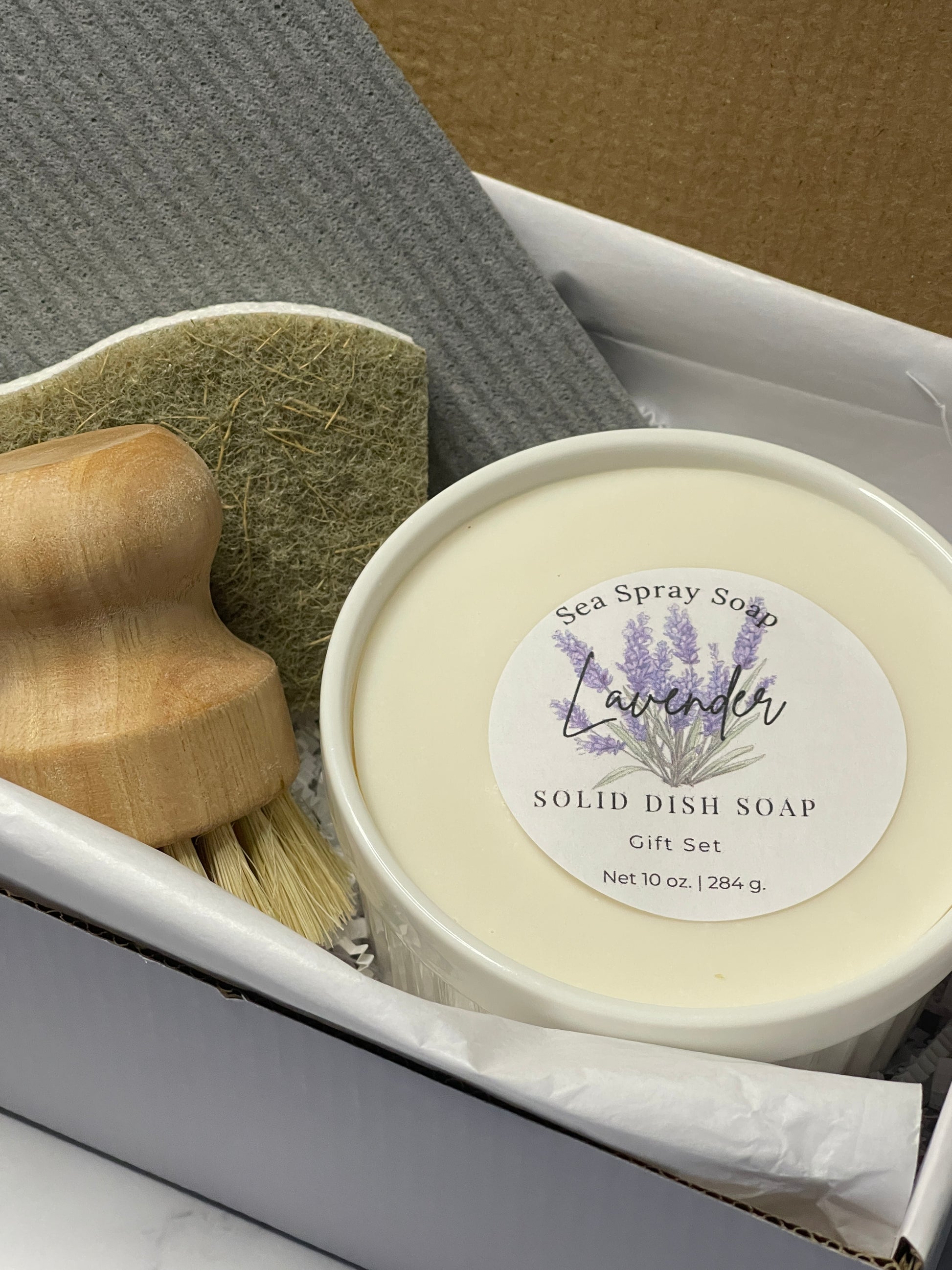 Solid dish soap with a label on top of a gray towel and wooden scrubber.