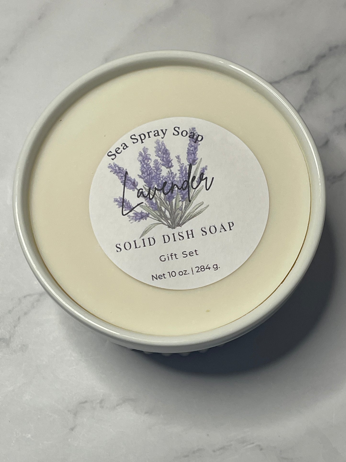 Solid dish soap in a round container with a label on a marble surface