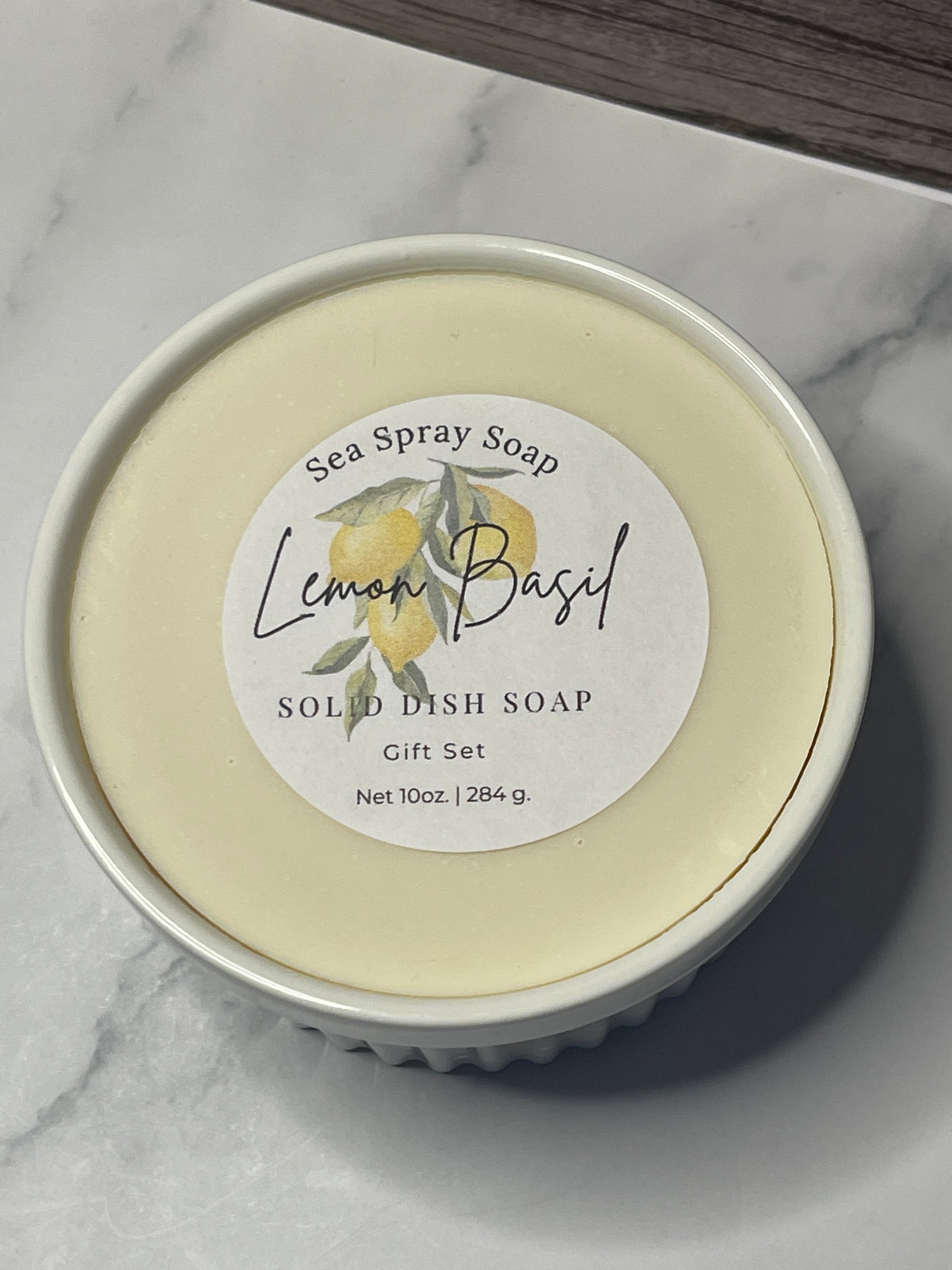 Solid dish soap in a container with a lemon basil label on a marble surface