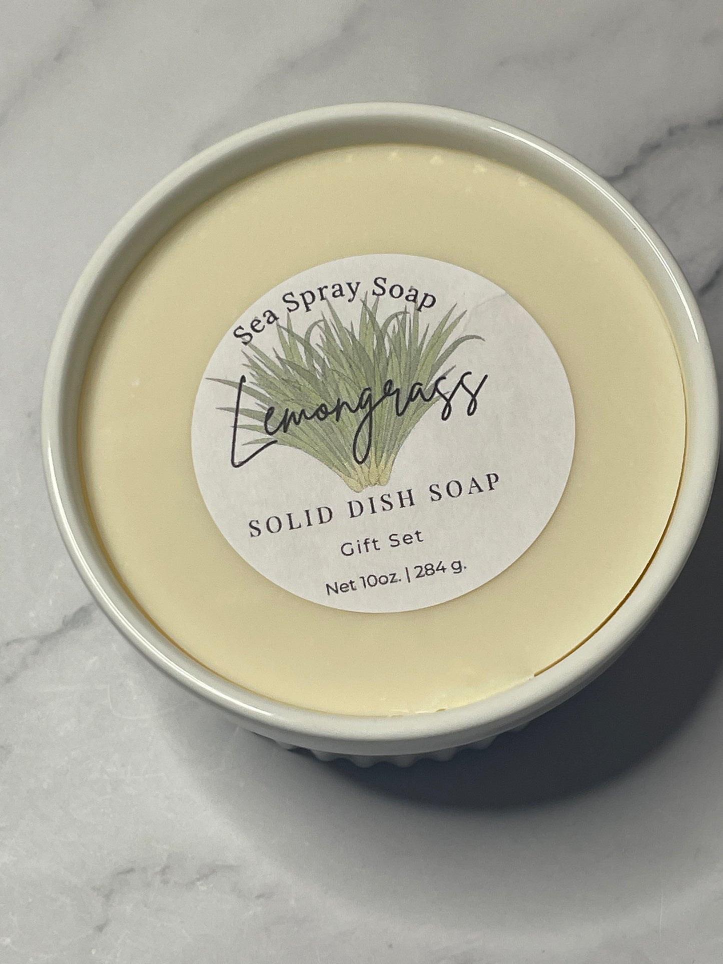 Solid dish soap in a container with a label on a marble surface