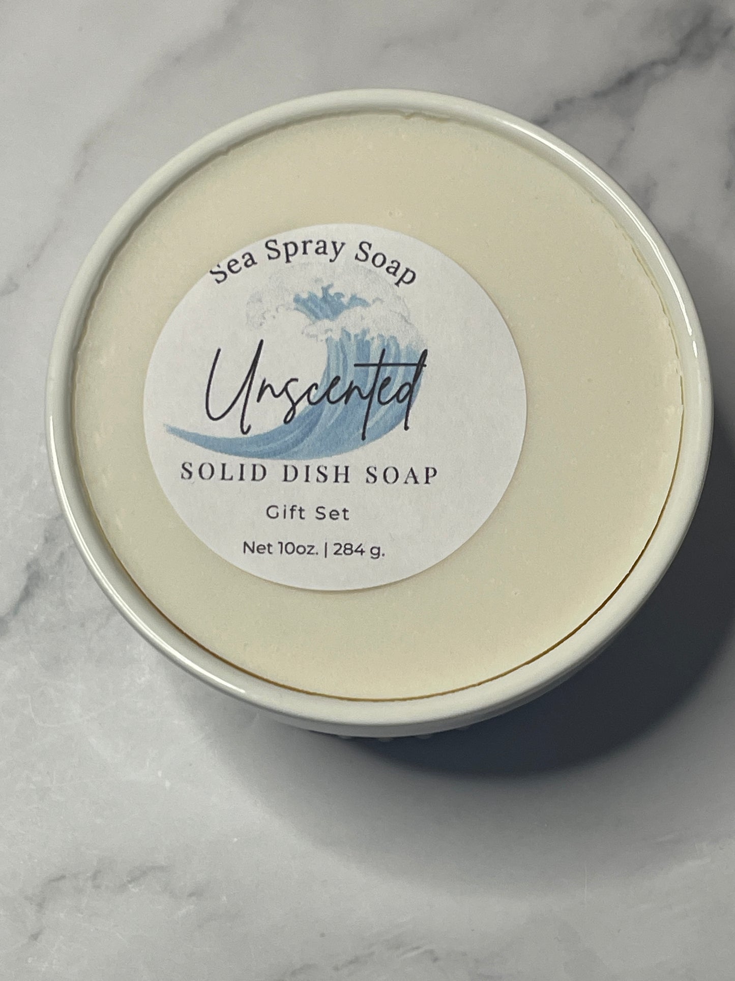 Solid dish soap in a container with a label on a marble surface